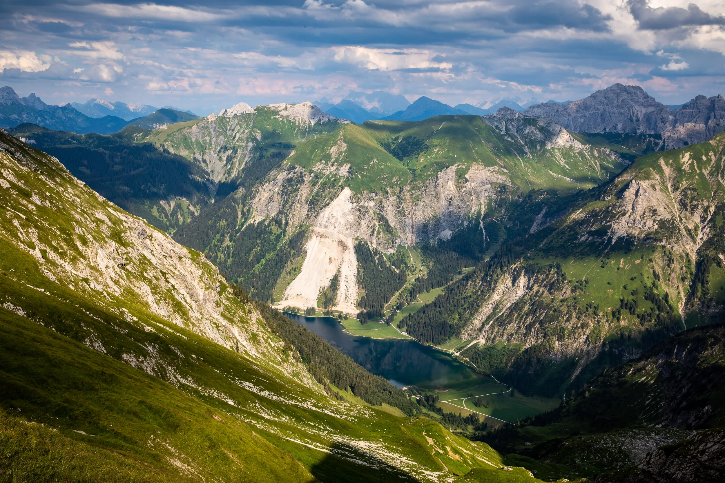 Blick über den Vilsalpsee unter gestaffelten Allgäuer Bergketten und einem wechselhaften Sommerhimmel