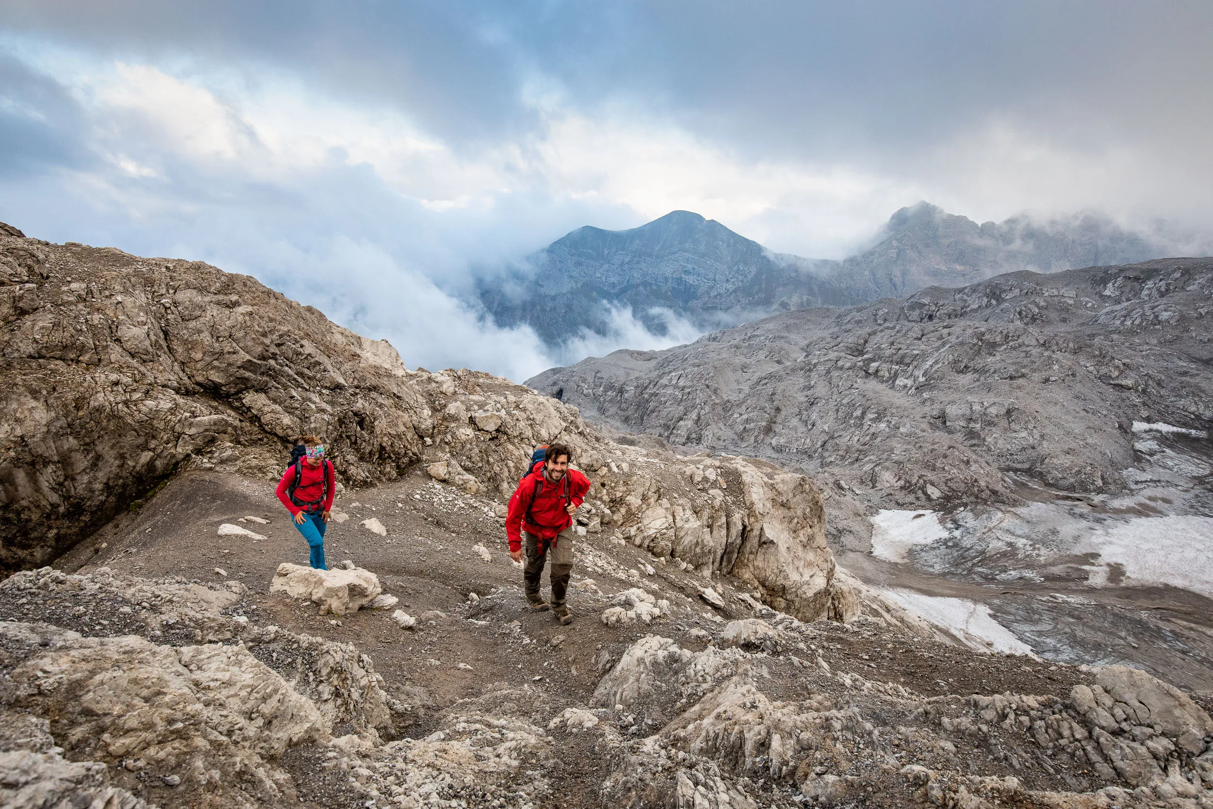 Raphaela Haug und Tom Besser steigen über gestuftes Kalkgestein vor dunklen Wolken