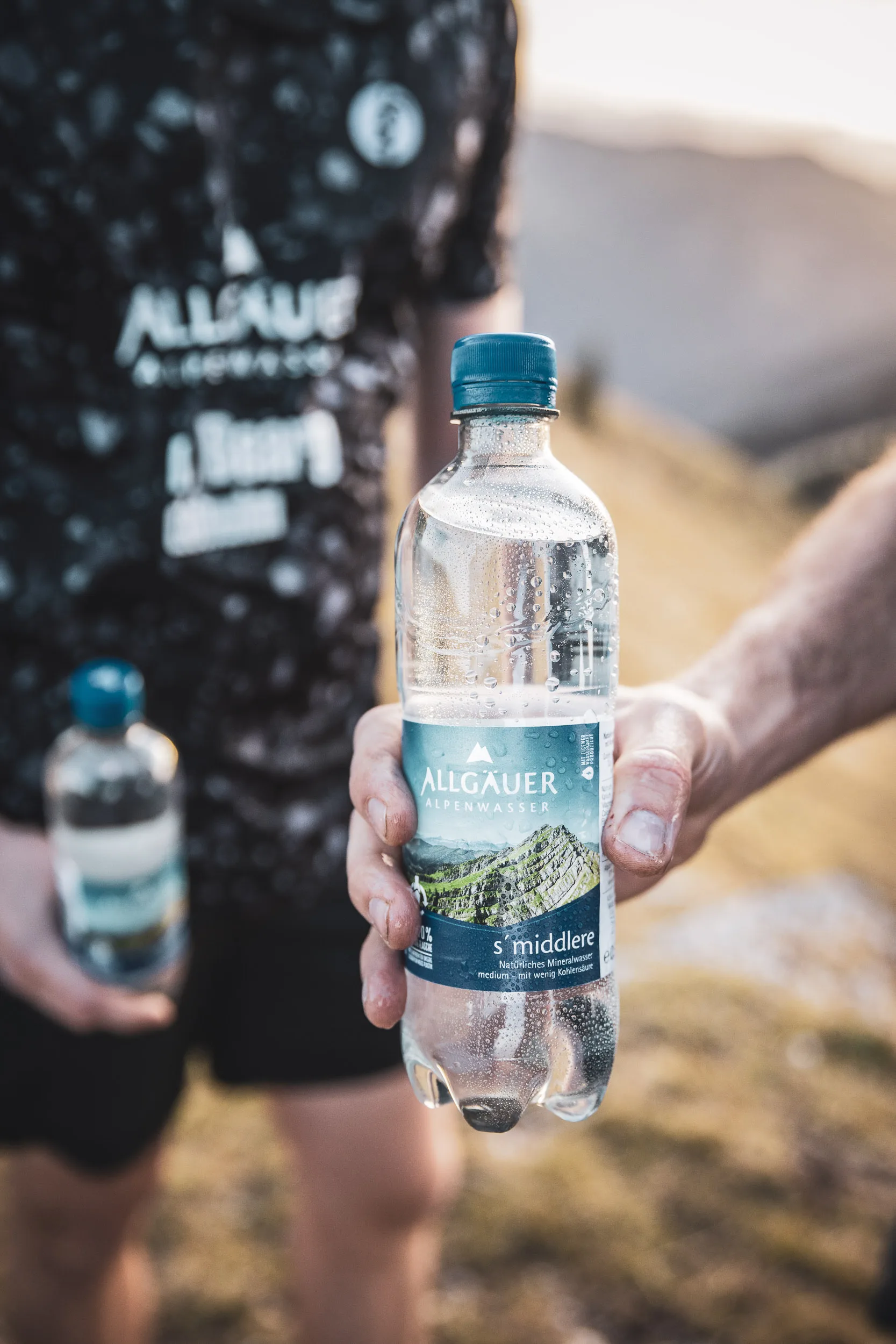 Mineralwasserflasche vor schwarzem Laufshirt und Berglandschaft