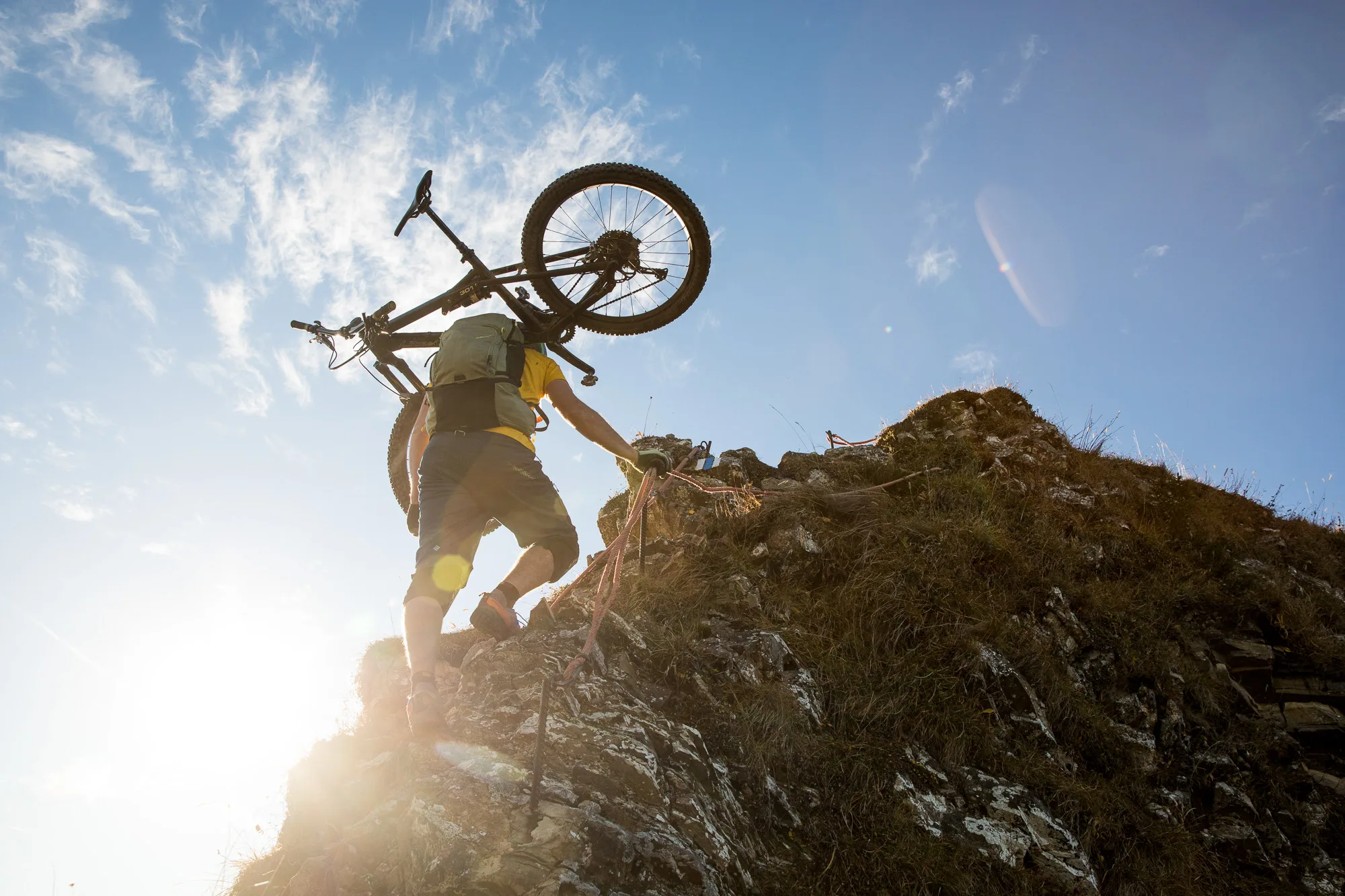Mountainbiker tragen ihre Räder an einem steilen Felsgrat vor hellem Himmel