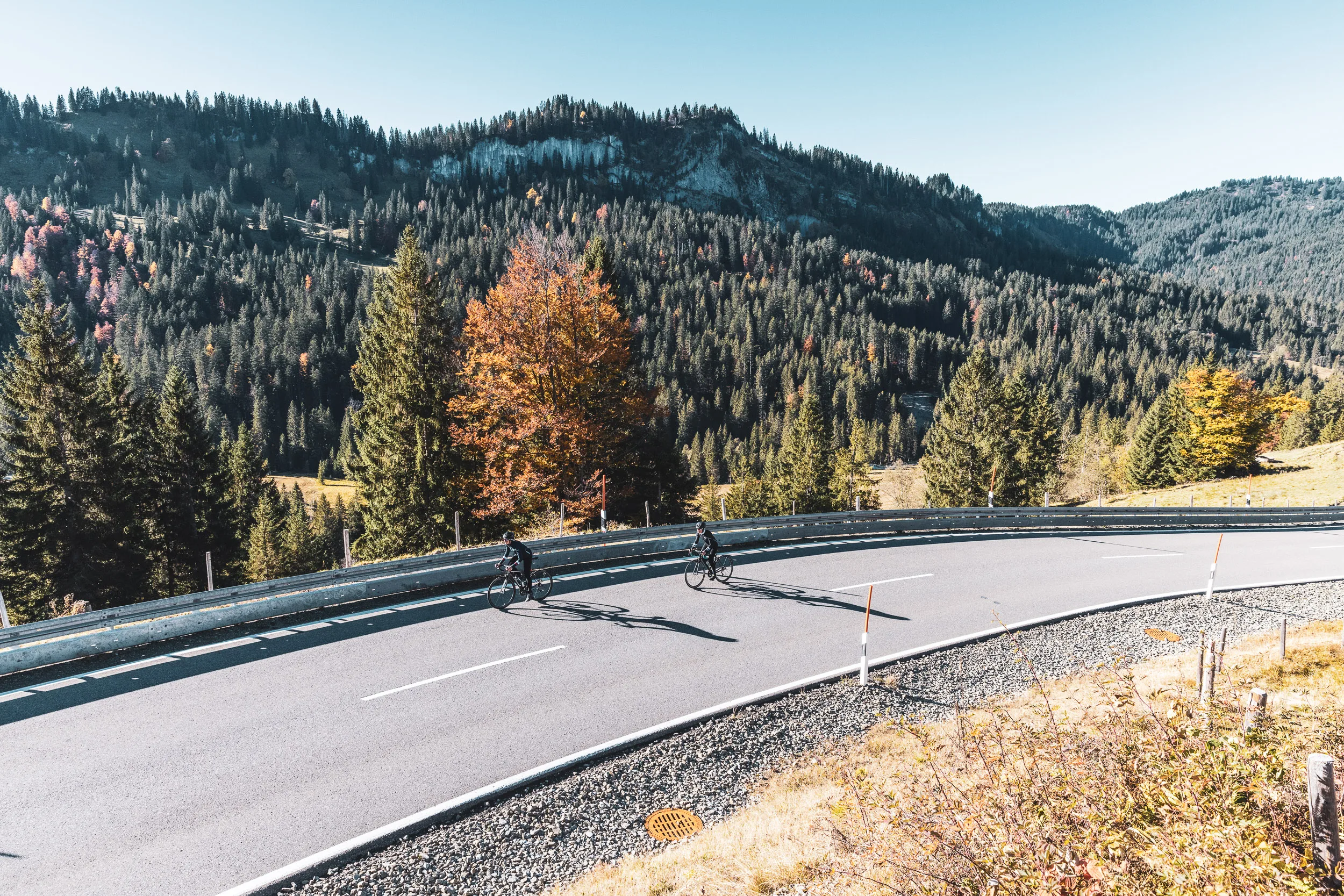 Rennradfahrerin auf einer kurvigen Passstraße vor herbstlichen Bergen