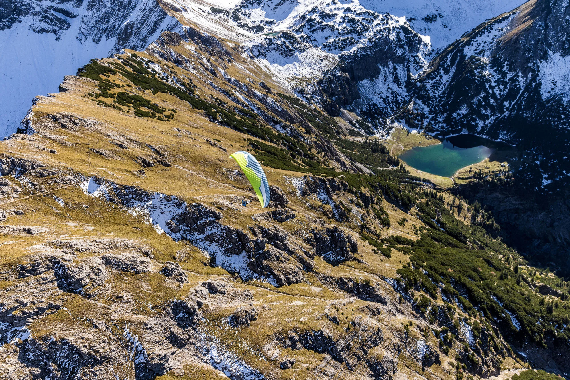 Michael Schnetzer zieht mit dem Gleitschirm über einen herbstlichen Felskamm bei Oberstdorf.