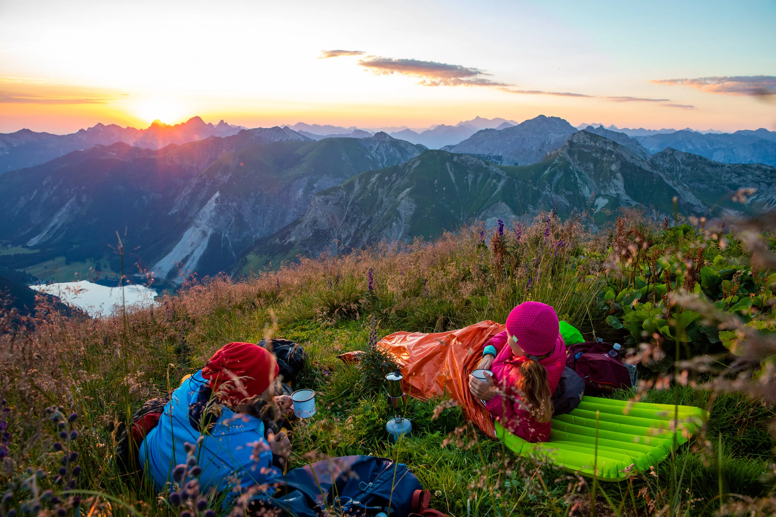 Caroline Nantke und Harald Dreyer liegen mit Schlafmatten auf einer Bergwiese bei Sonnenuntergang