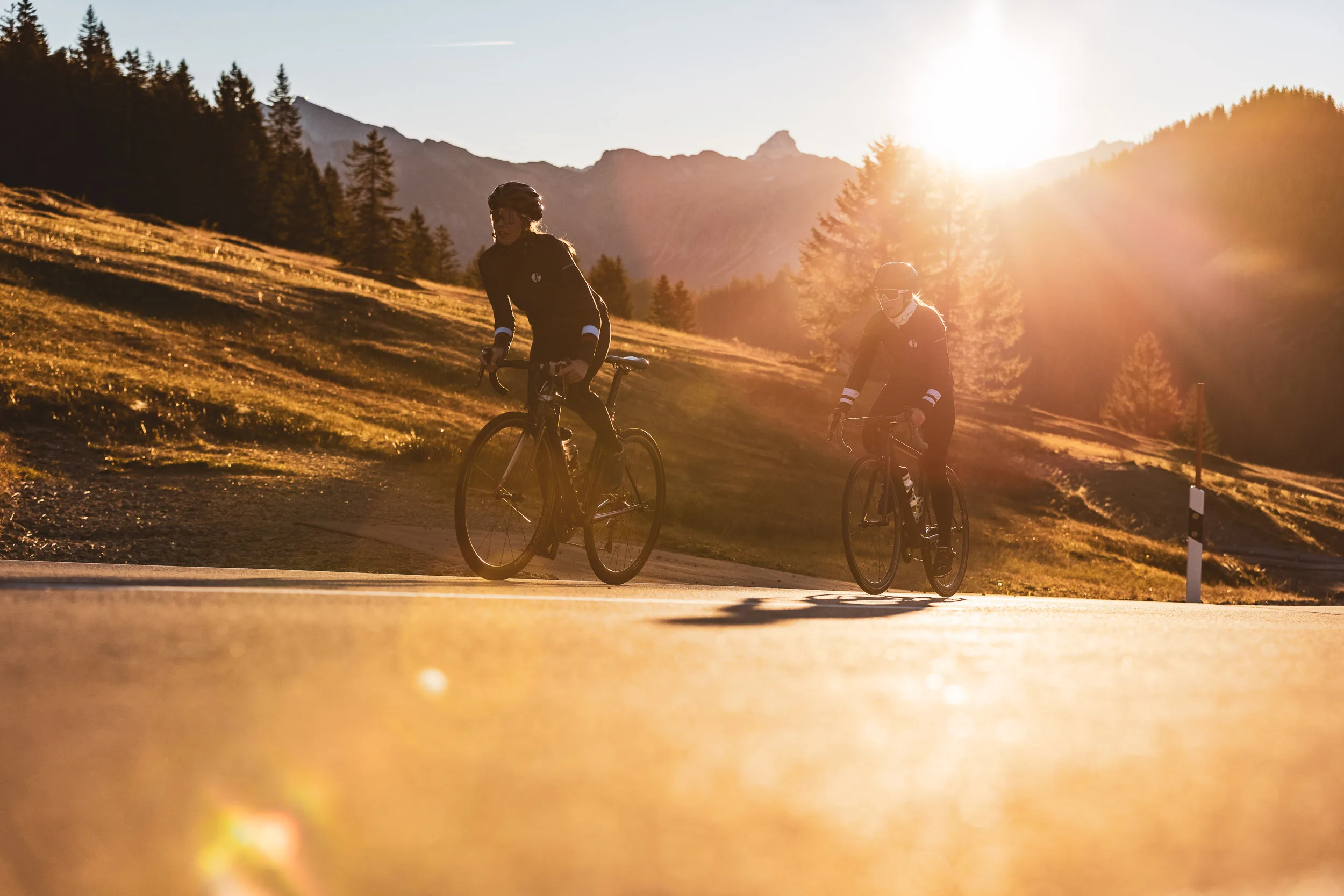 Zwei Rennradfahrerinnen auf der Passstraße vor herbstlichen Wiesen