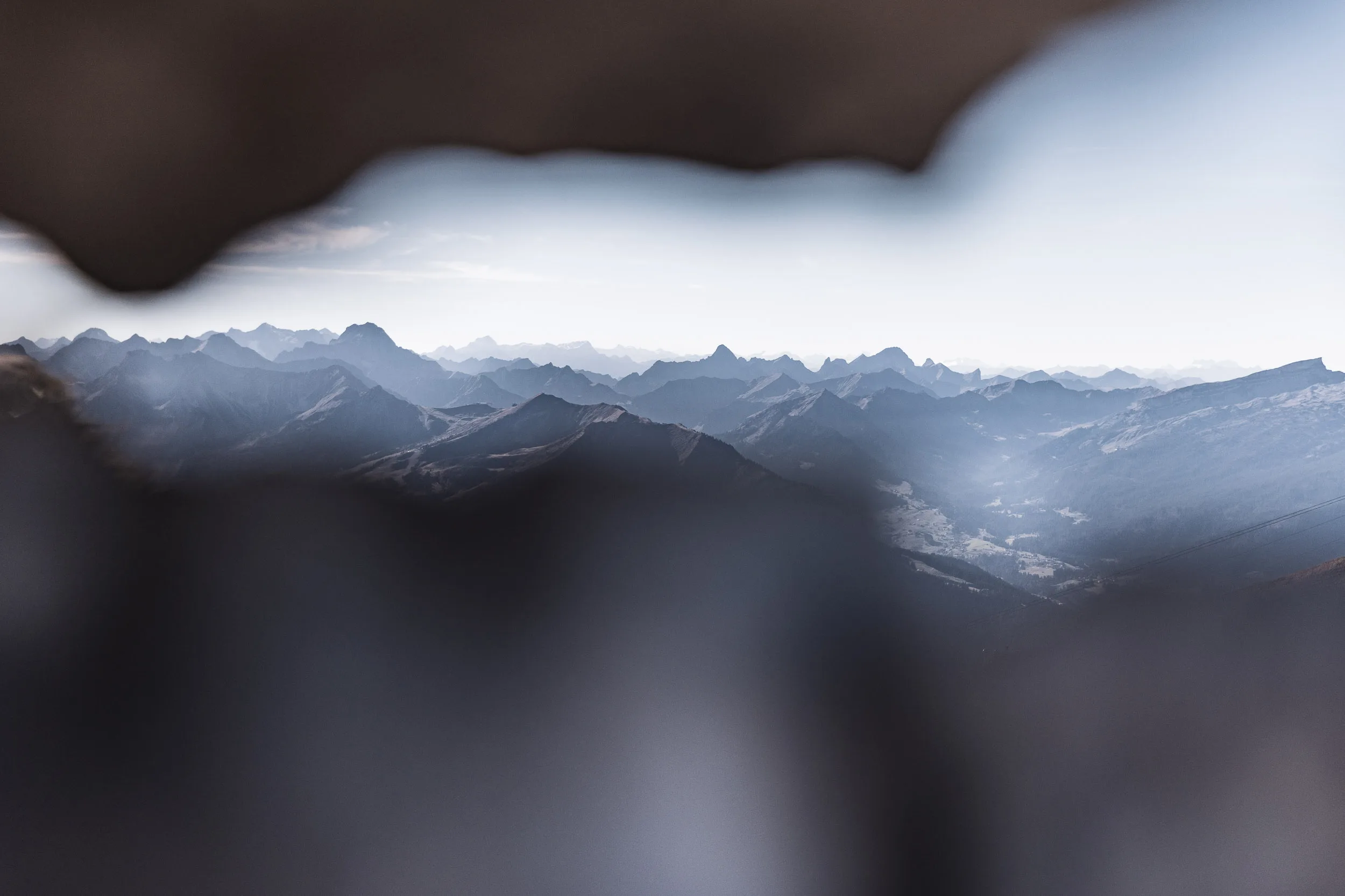 Unscharfe Felsen rahmen den Blick auf gestaffelte Gipfel und ein fernes Tal.