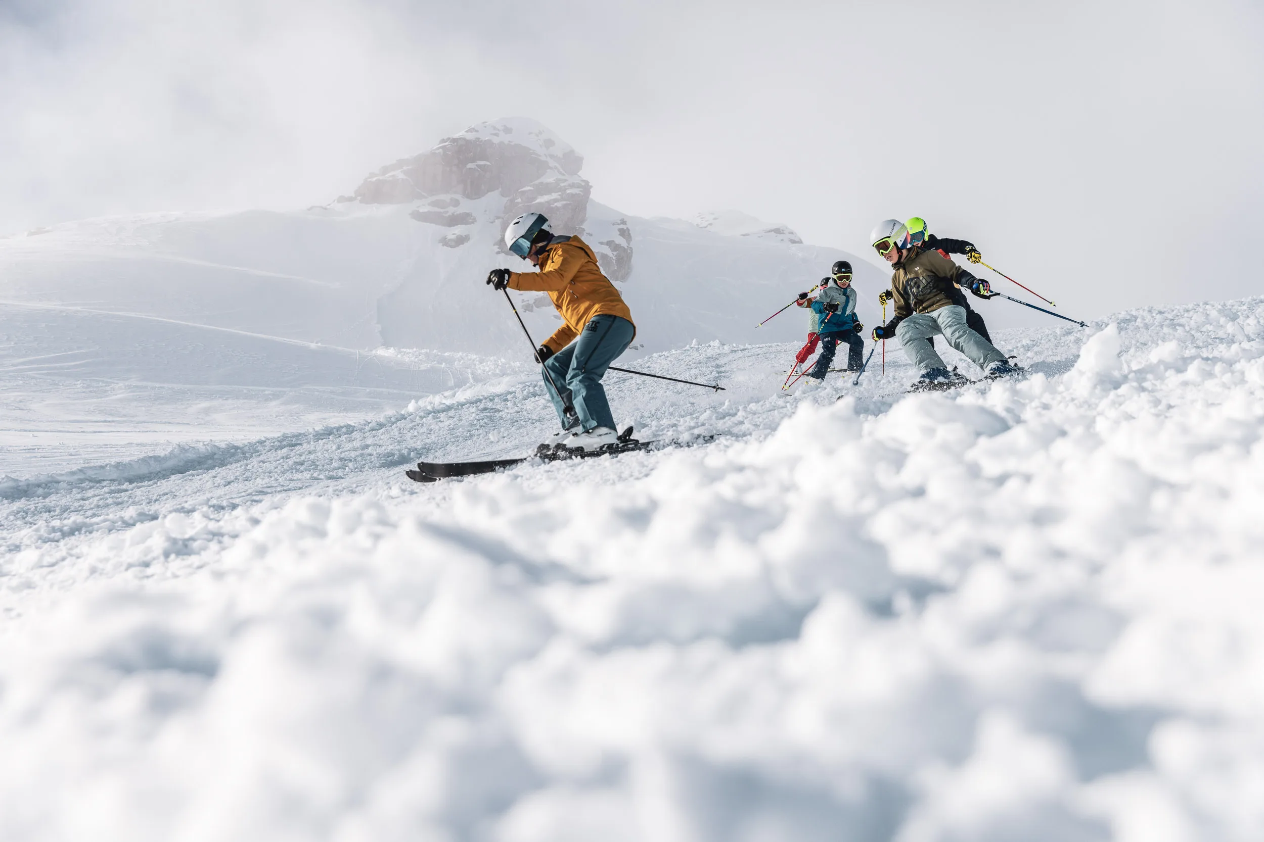 Skilehrer und Gruppe fahren durch aufgewirbelten Schnee am Hang