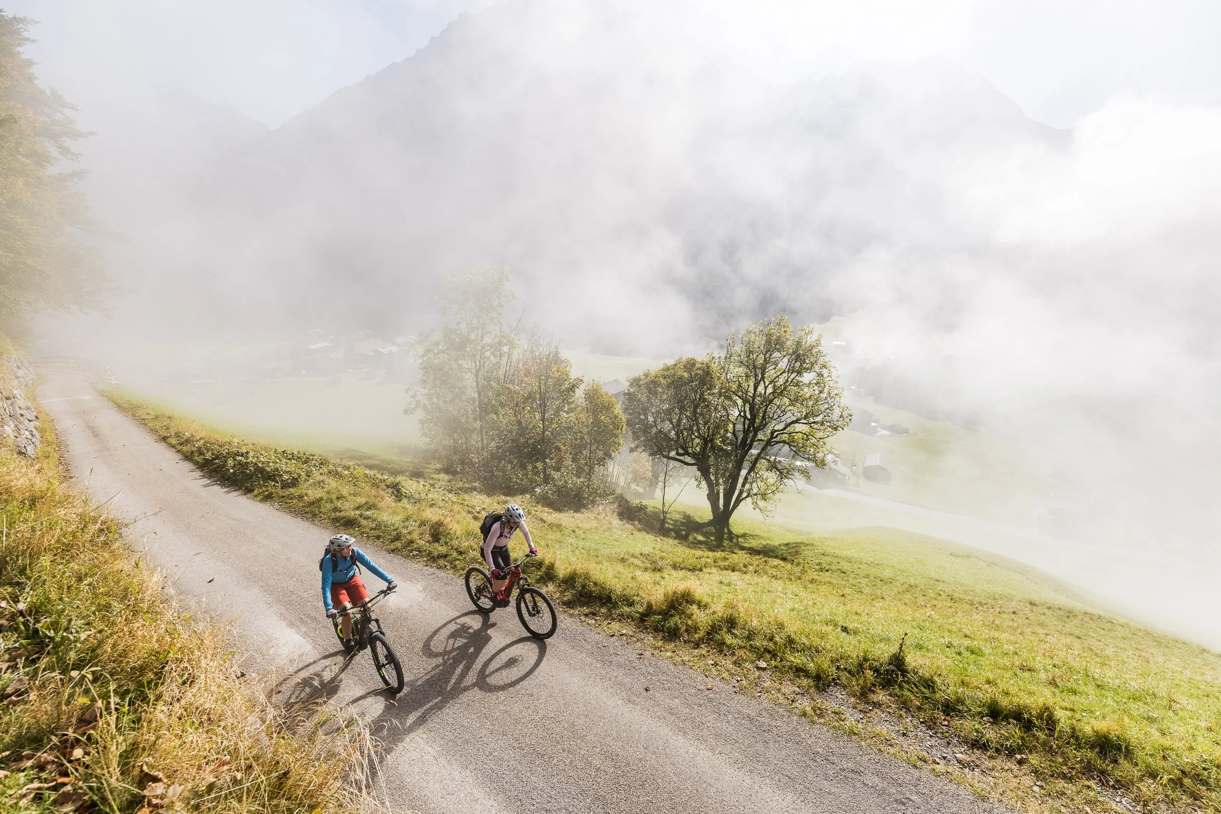 Silvi Vogel und Andrea Geiger fahren mit Mountainbikes durch Nebel über dem Kleinwalsertal