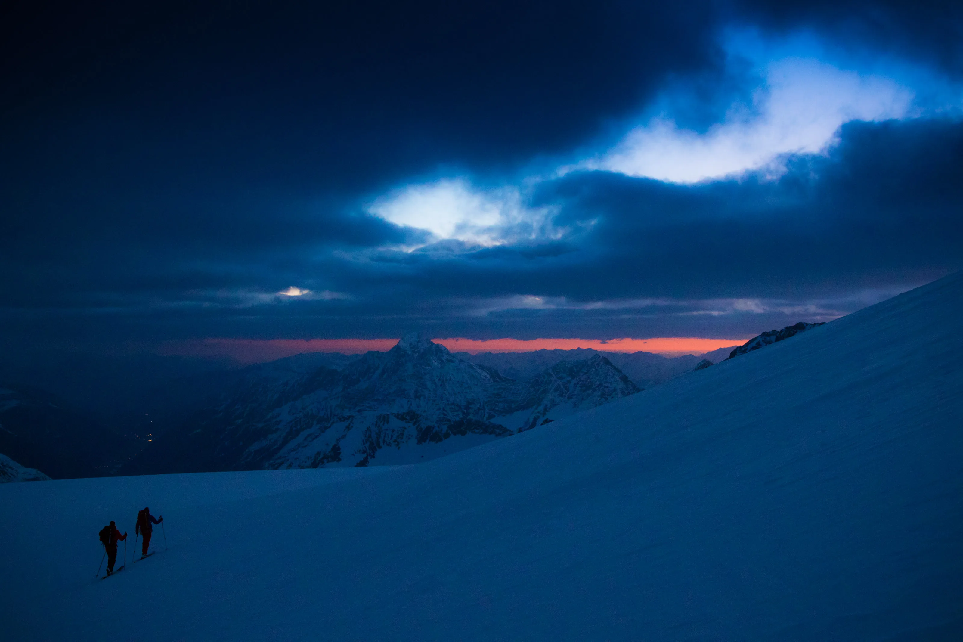 Zwei Skitourengeher steigen im blauen Morgenlicht über einen verschneiten Hang am Stubaier Gletscher