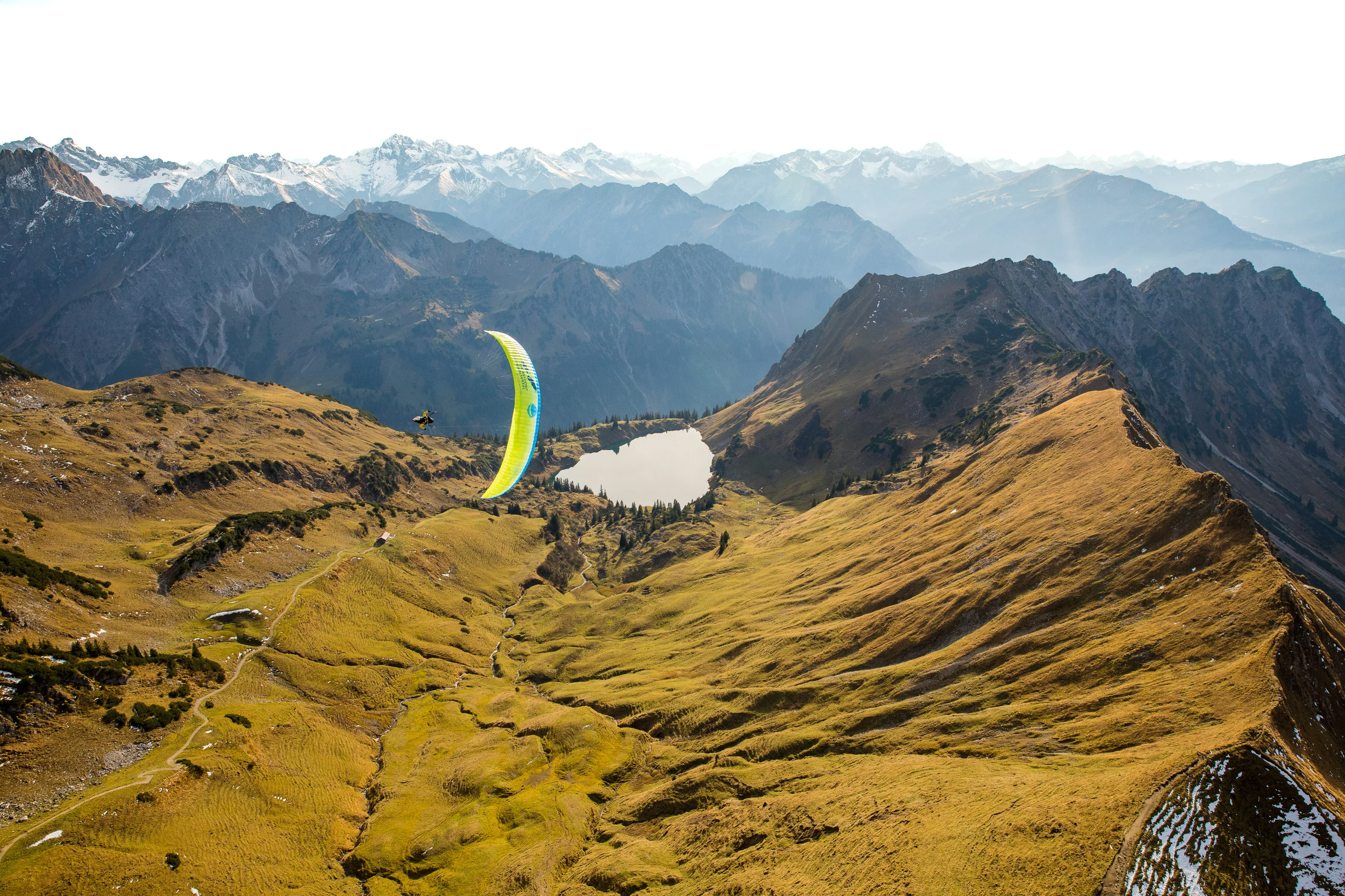 Michael Gebert fliegt mit grünem Gleitschirm über herbstliche Grate und den Seealpsee am Nebelhorn