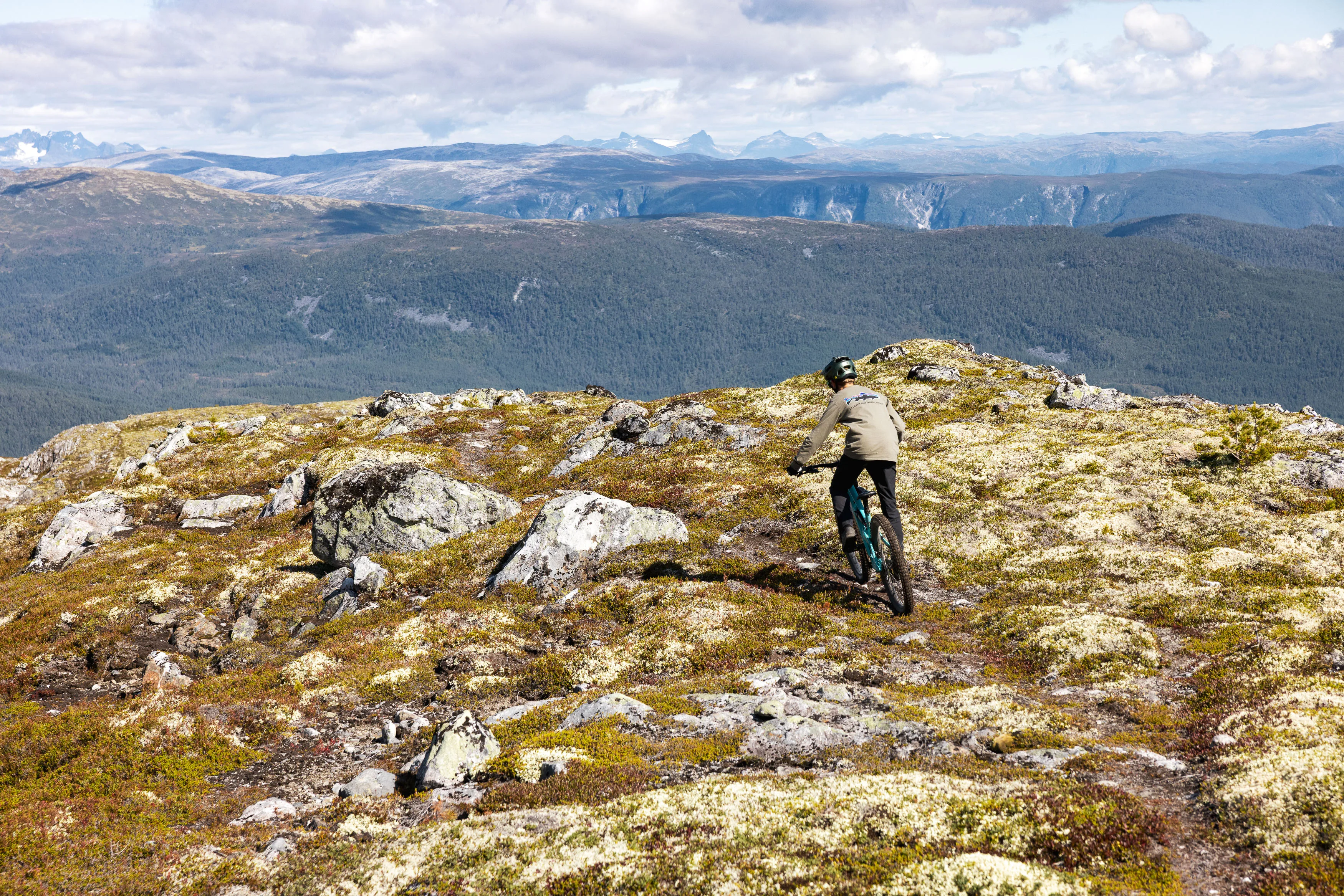 Mountainbiker fährt über grobes Felsgelände in Richtung bewaldetes Fjordtal