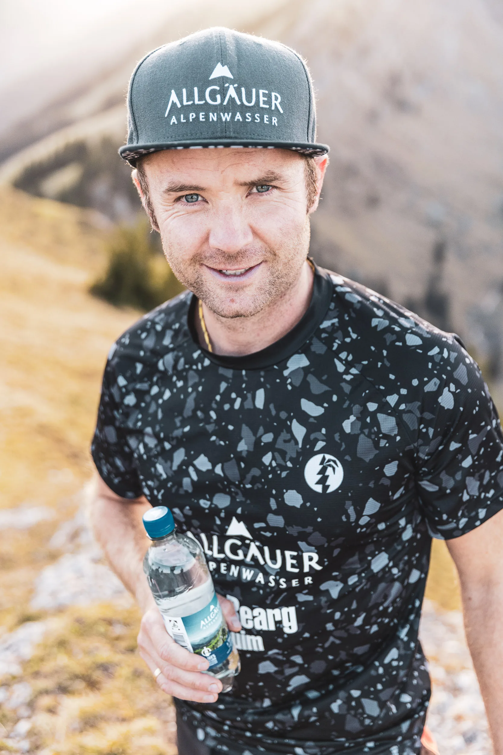 Trailrunner mit Trinkflasche auf einem Bergpfad im warmen Licht