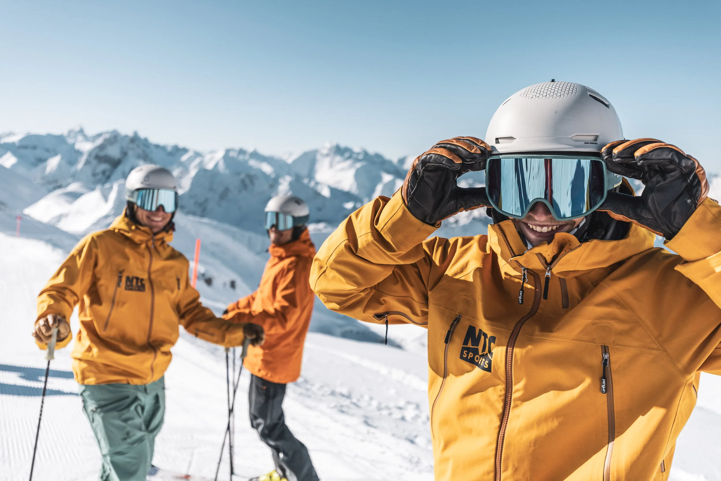 Skilehrer richtet seine Skibrille, zwei Kollegen stehen dahinter
