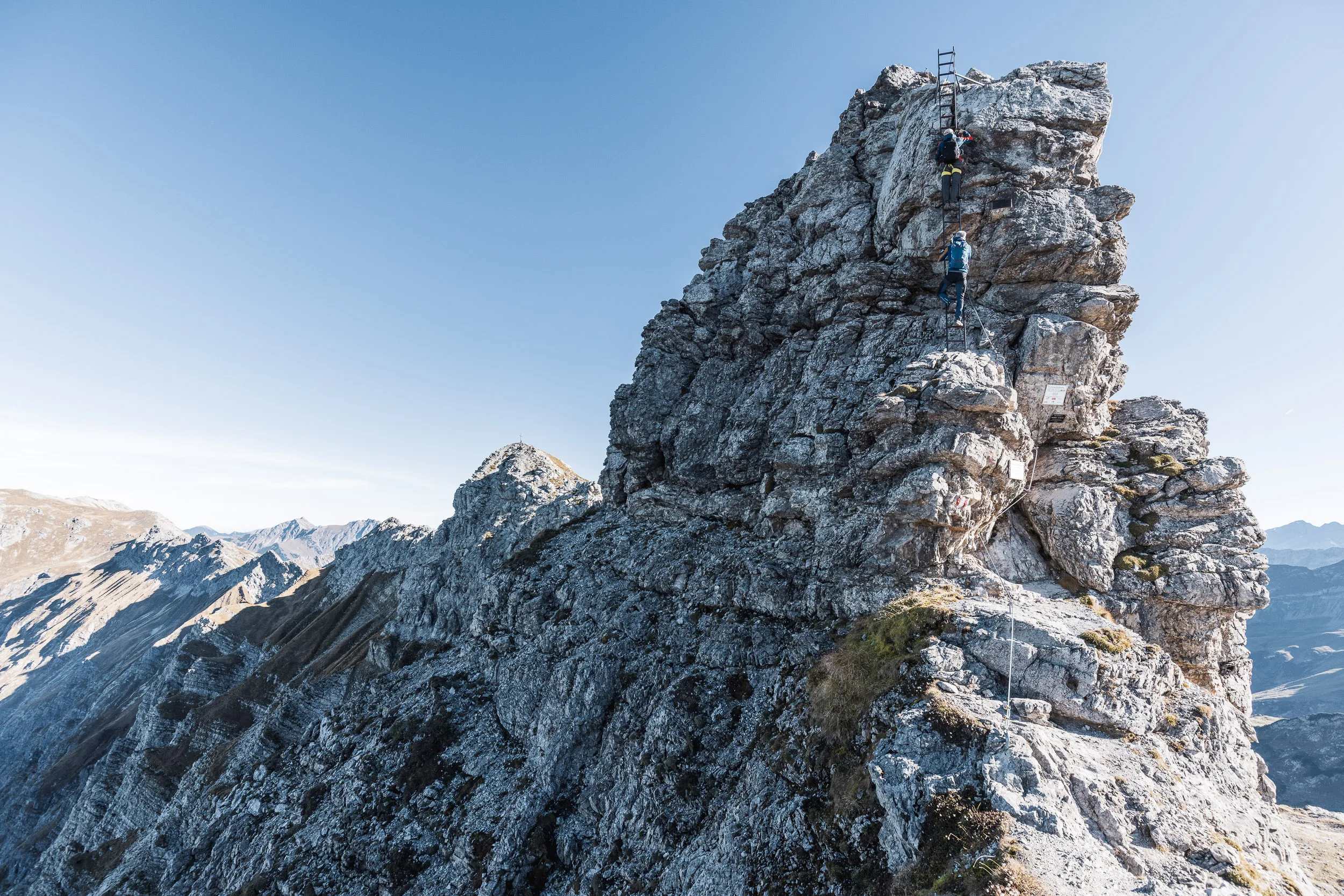Zwei Bergsteiger steigen nacheinander über Leitern durch einen steilen Felsturm.