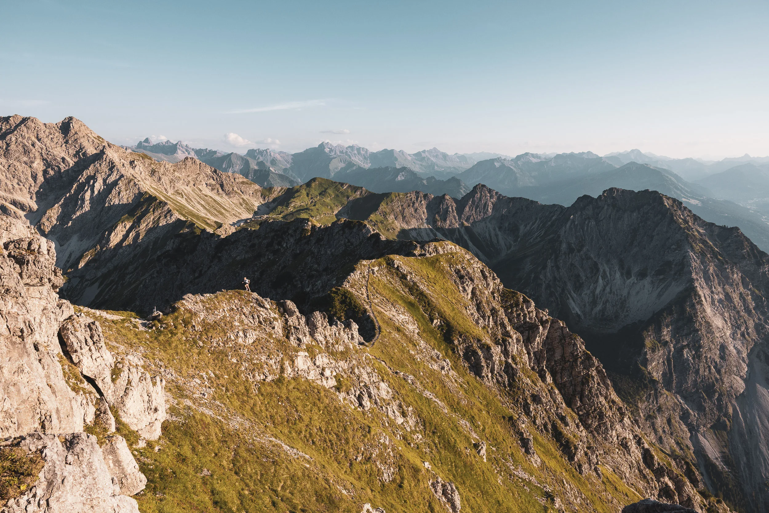 Grüne und felsige Berggrate vor einem weiten Alpenpanorama