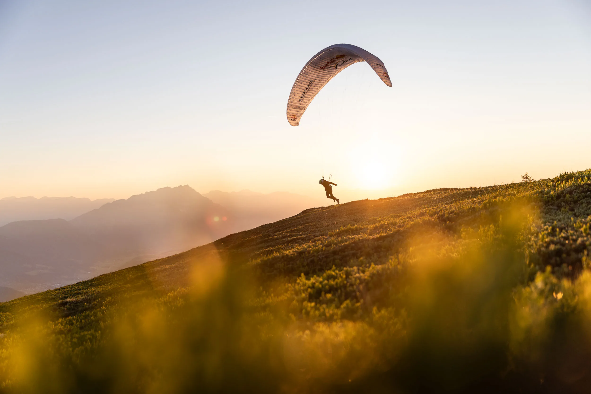 Gleitschirmpilotin mit aufgezogenem Schirm auf einem Bergruecken im ersten Morgenlicht