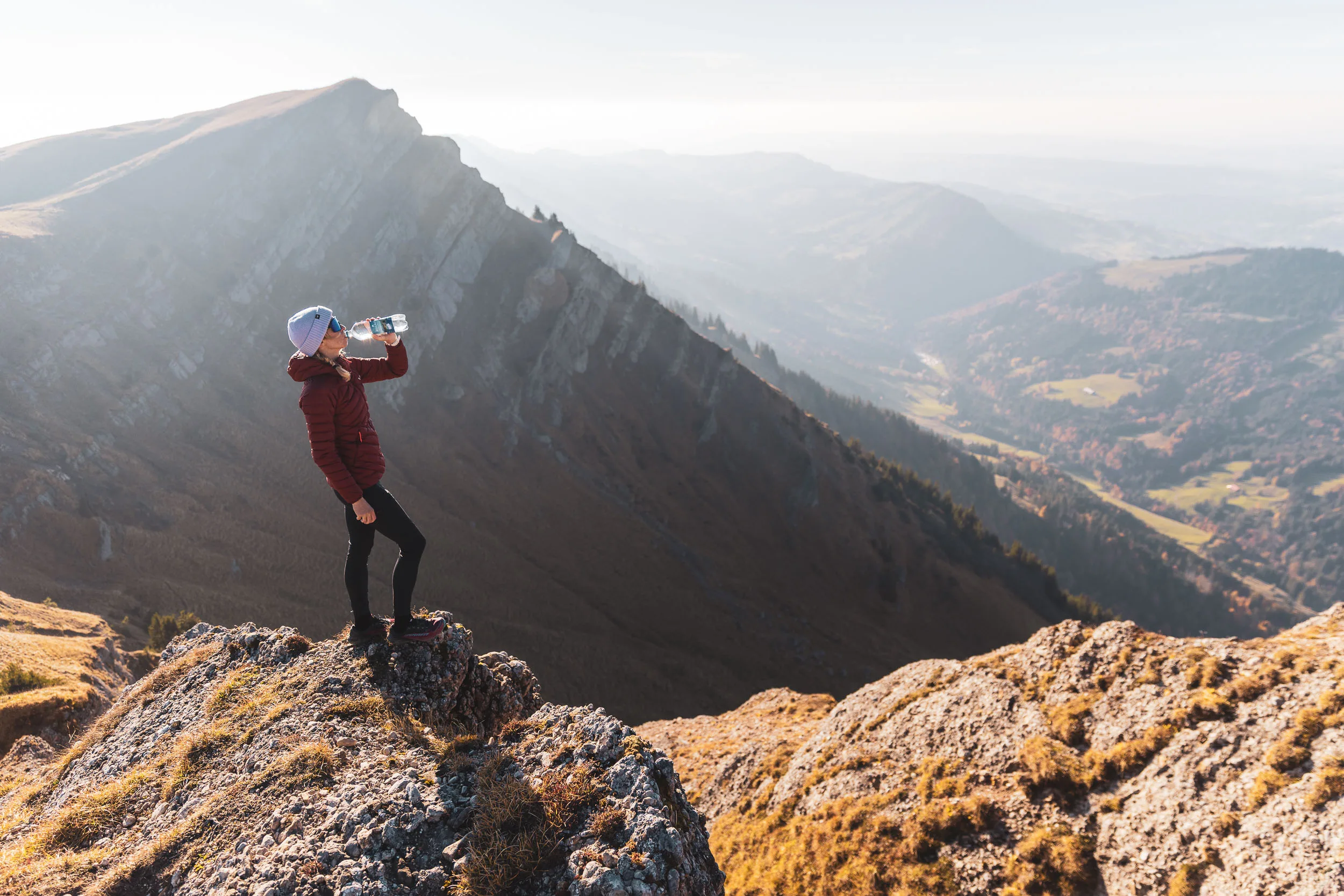 Wanderin trinkt auf einem Felsen mit weitem Blick über Grat und Allgäuer Tal