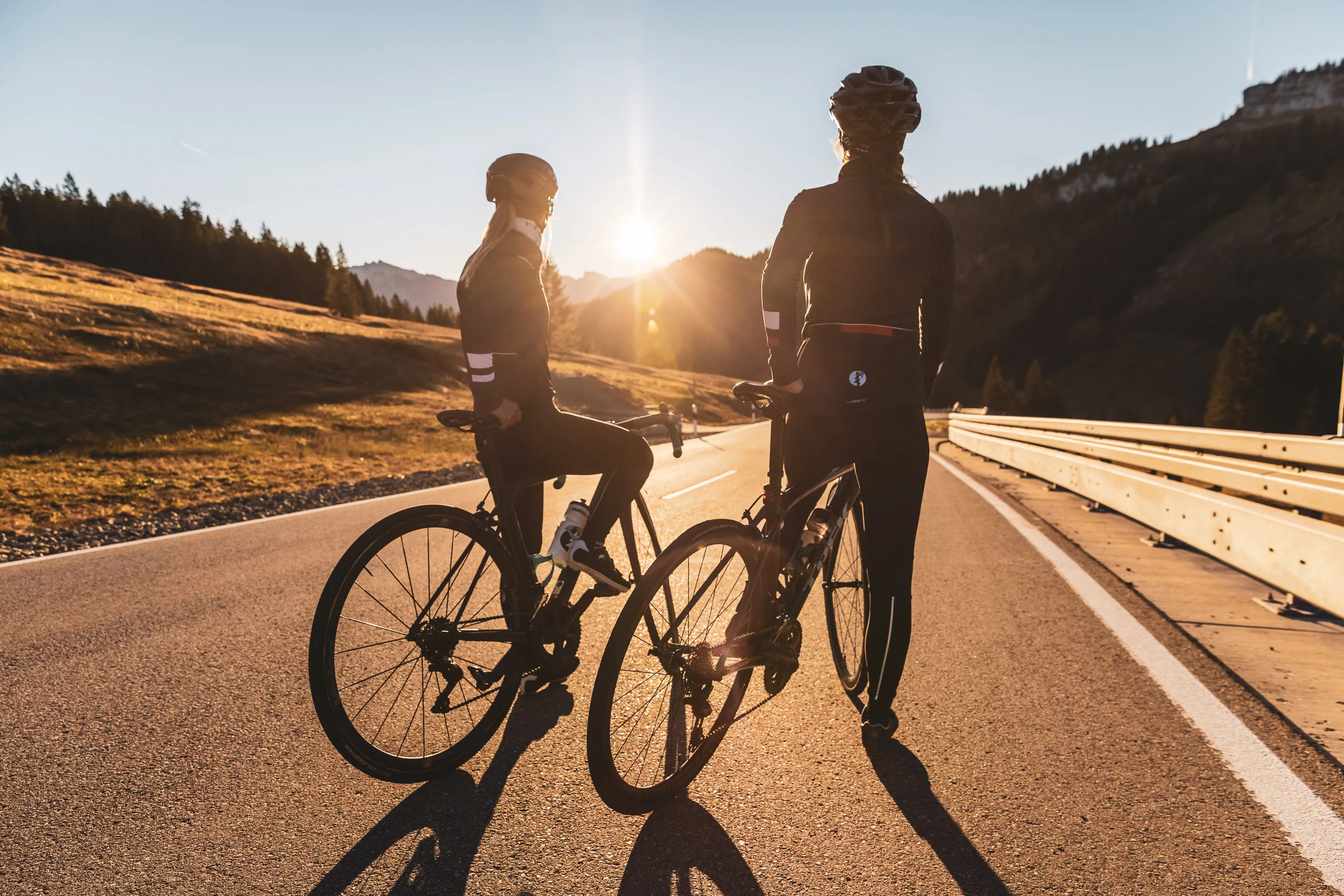 Zwei Rennradfahrerinnen stehen mit ihren Rädern im warmen Abendlicht