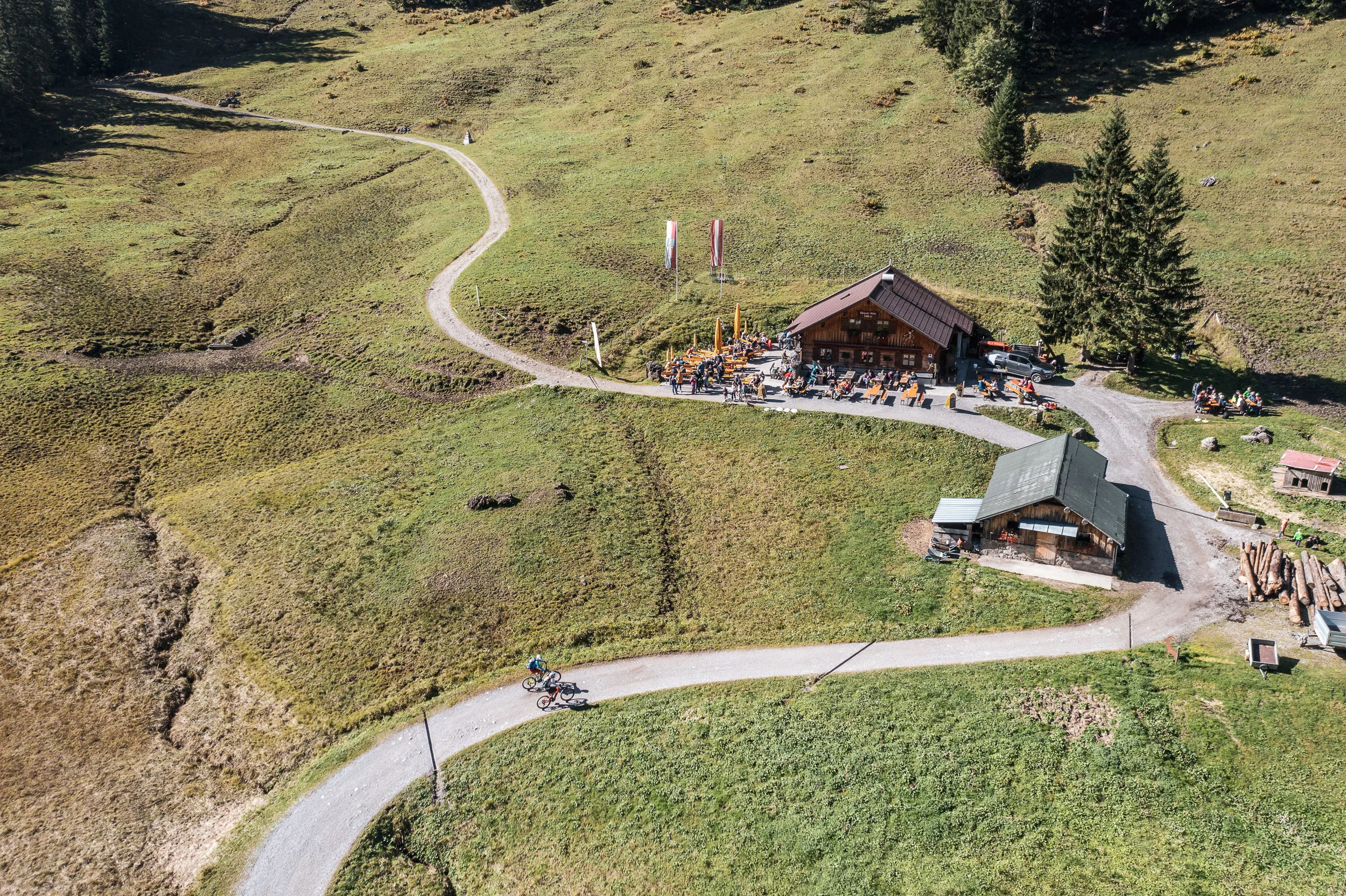 Luftaufnahme eines Berggasthauses mit Mountainbikerinnen auf der Zufahrt im Kleinwalsertal