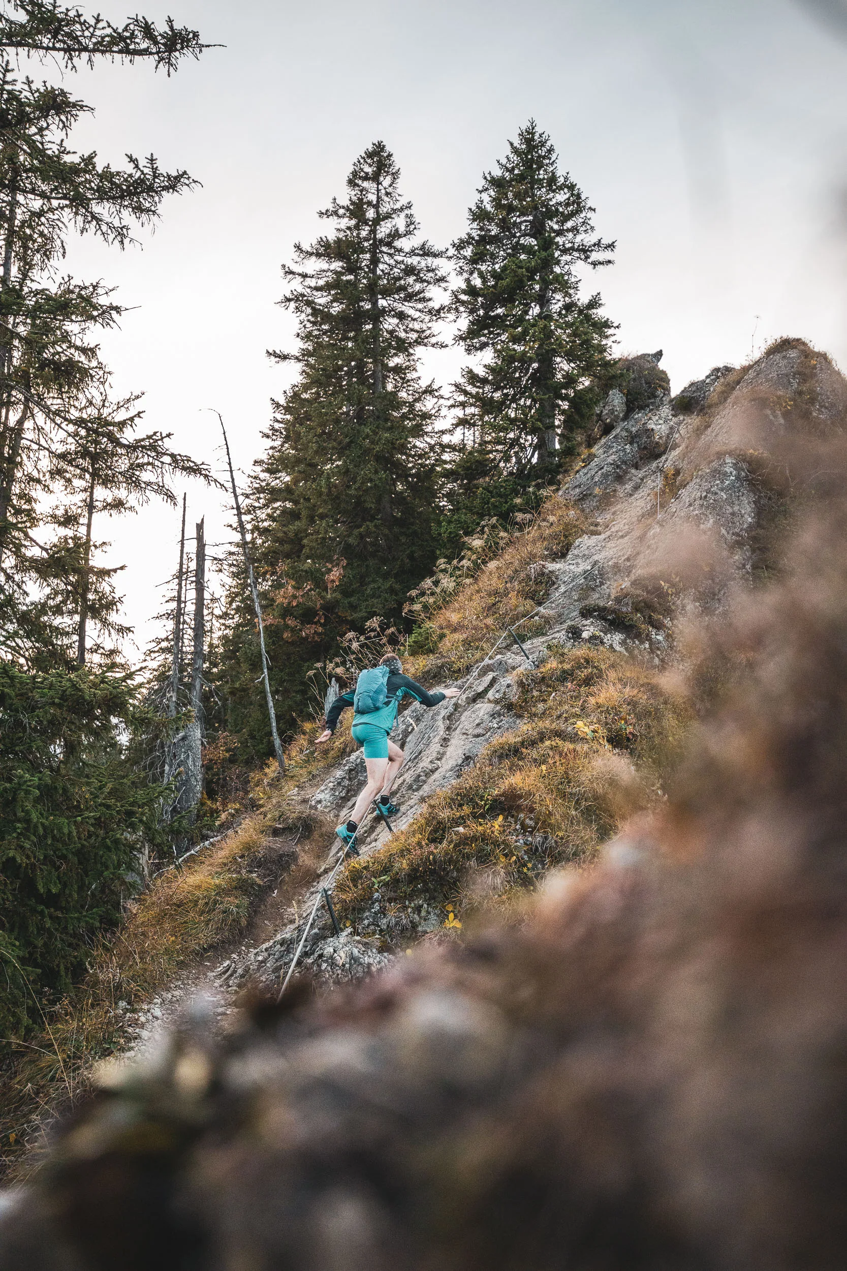Andreas Kögel steigt beim Trailrunning über einen felsigen Abschnitt zwischen hohen Fichten.