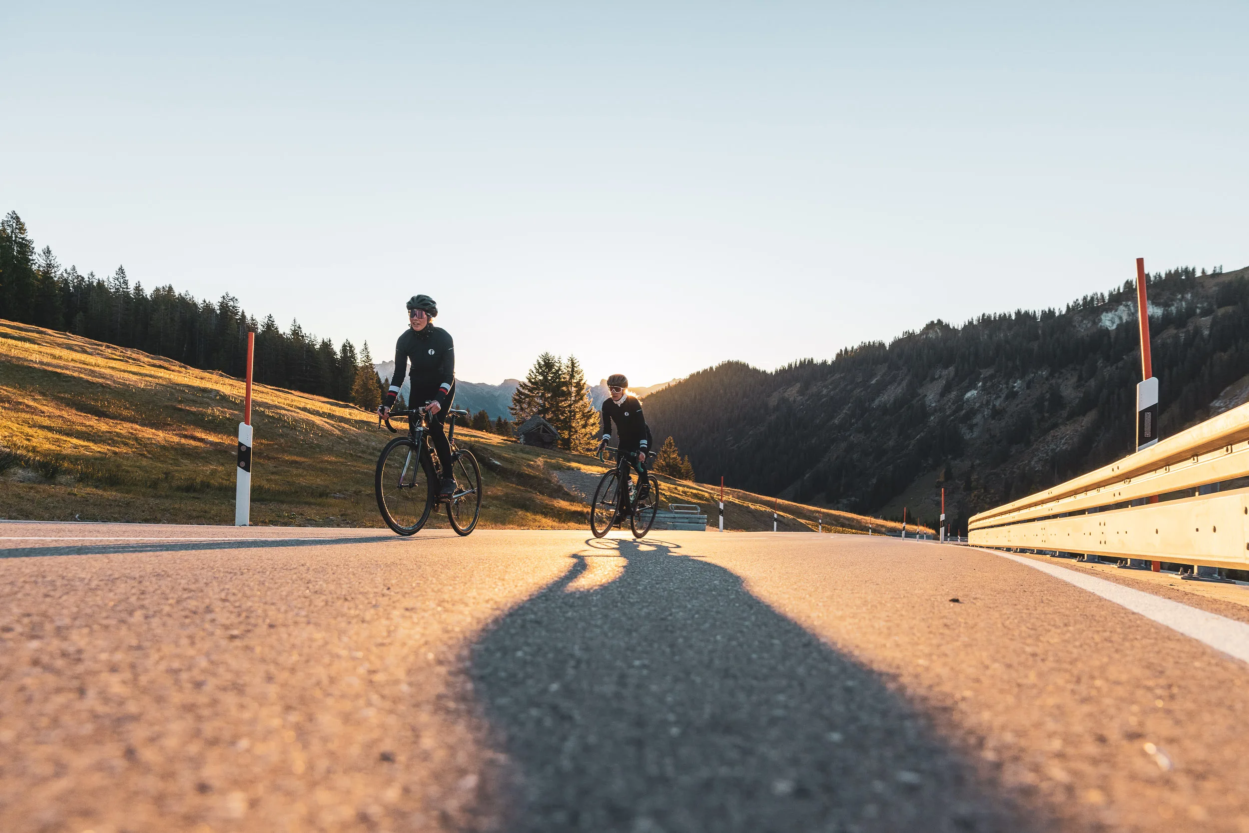 Zwei Rennradfahrerinnen mit langen Schatten auf dem Asphalt im Abendlicht