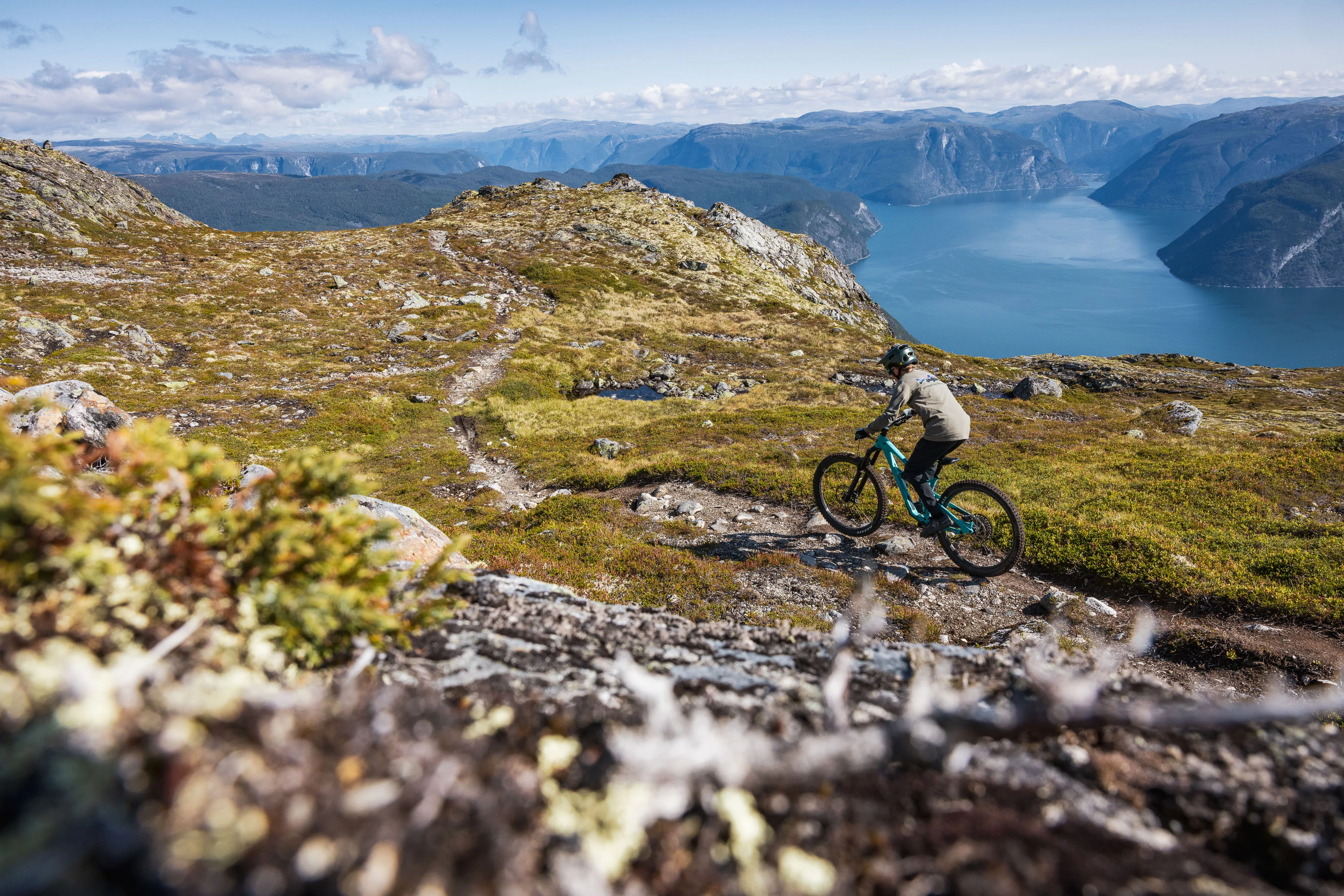 Mountainbiker fährt durch eine Kurve auf einem felsigen Hang mit weitem Fjordblick