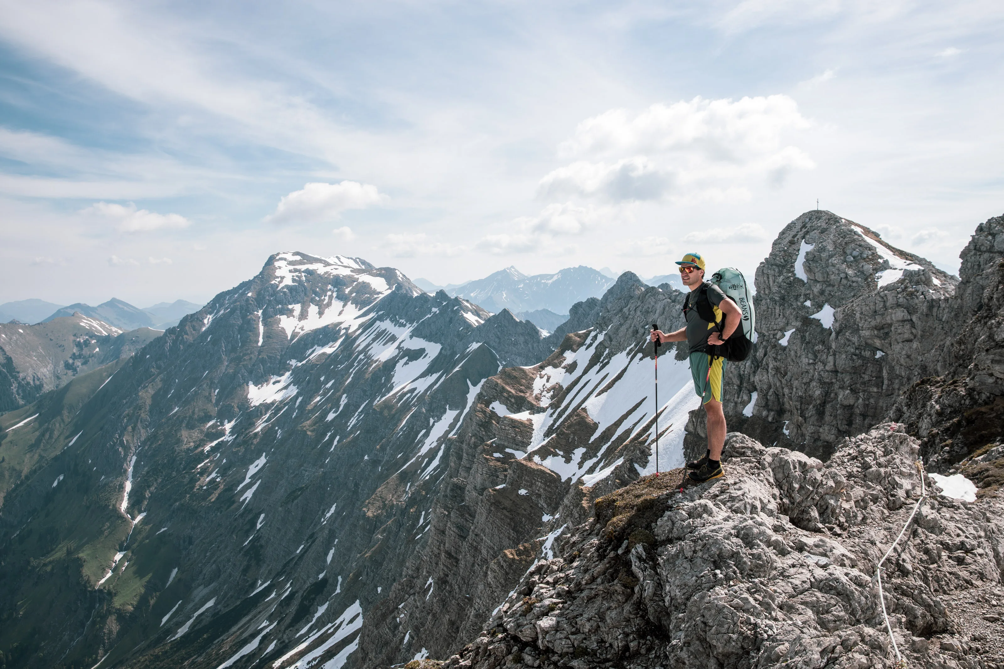 Michael Lacher steigt über helle Felsen; hinter ihm öffnen sich die schneebedeckten Allgäuer Gipfel.