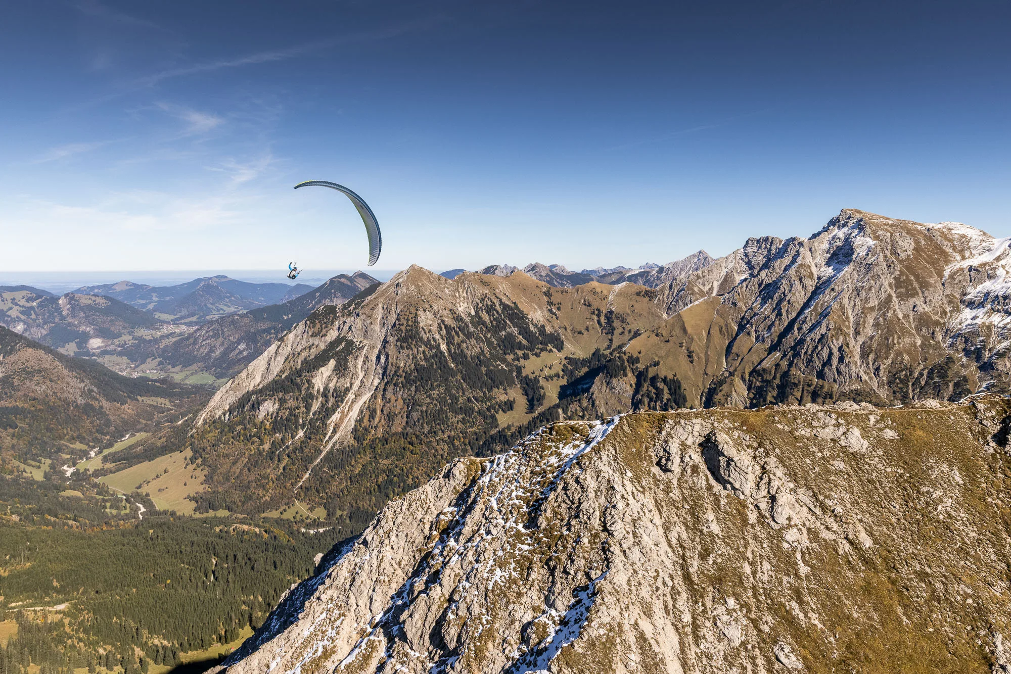 Michael Schnetzer fliegt mit dem Gleitschirm über den herbstlichen Bergen bei Oberstdorf.