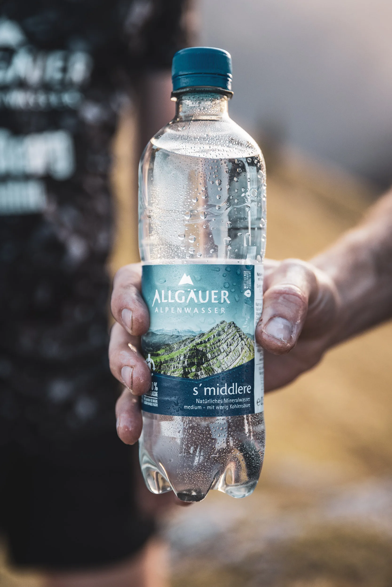 Mineralwasserflasche in einer Hand vor unscharfer Bergkulisse