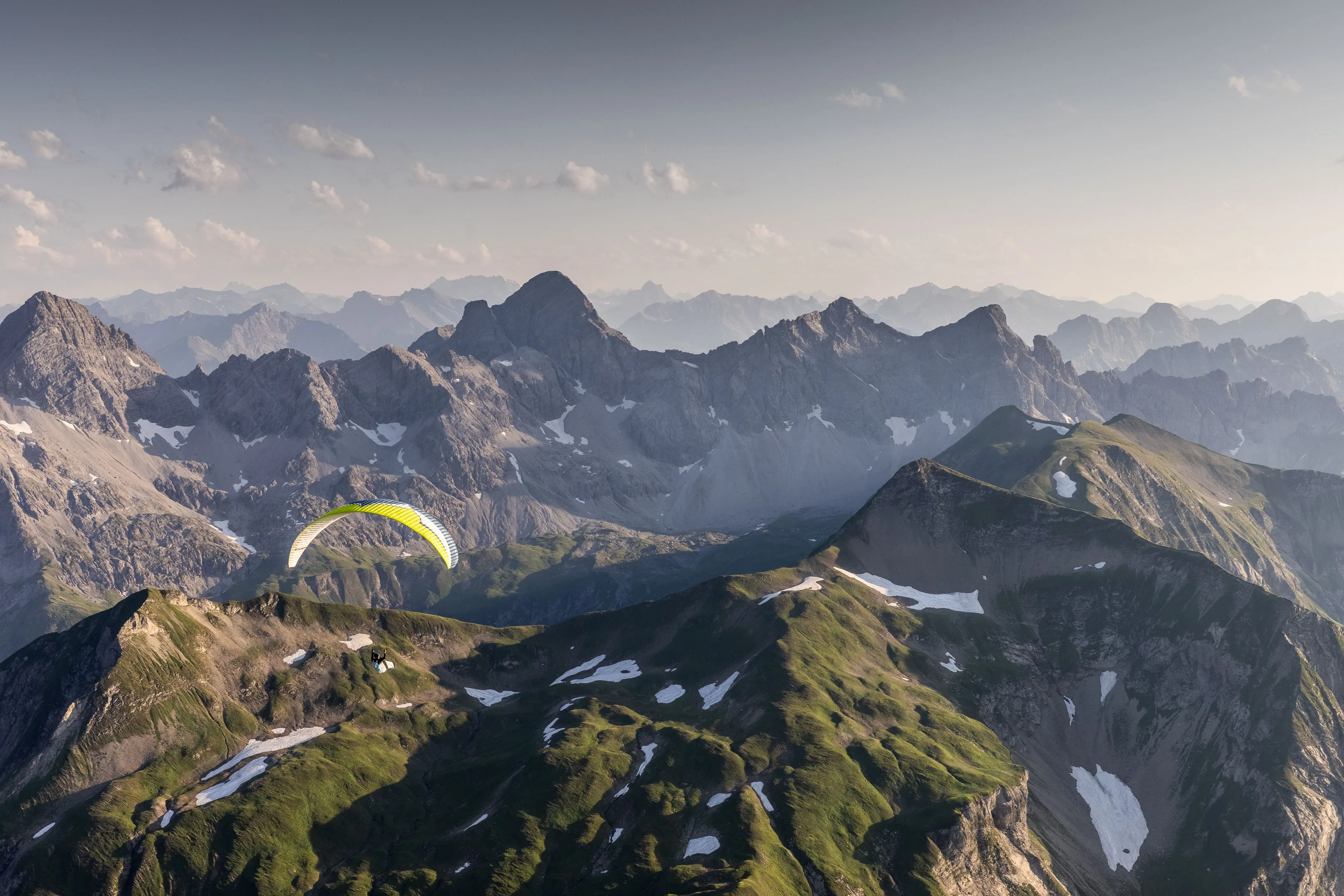 Ein Gleitschirm folgt der Kontur eines Berggrats vor einer zerklüfteten Gipfelkette