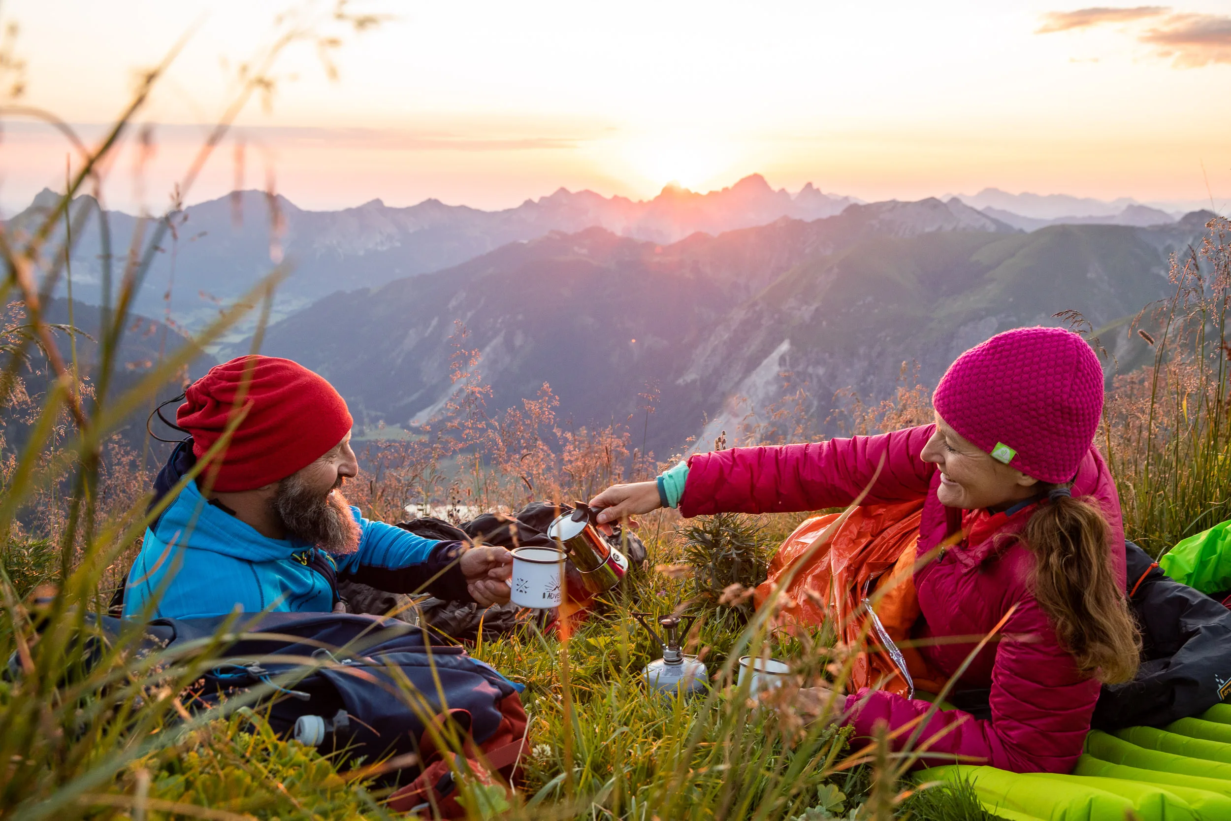 Caroline Nantke und Harald Dreyer trinken auf einer Bergwiese vor dem Sonnenuntergang