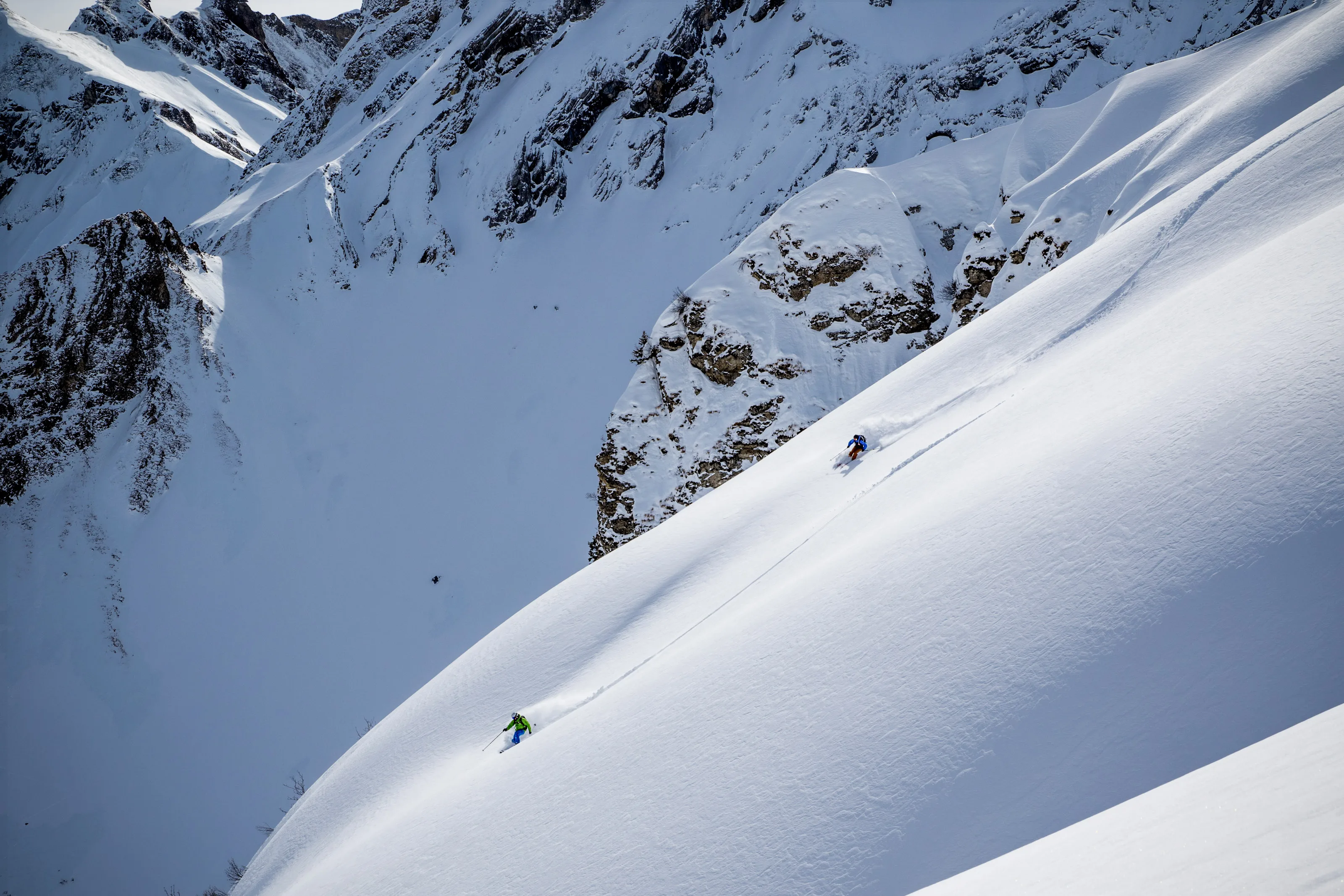Zwei Skifahrer fahren durch steiles, verschneites Gelände.