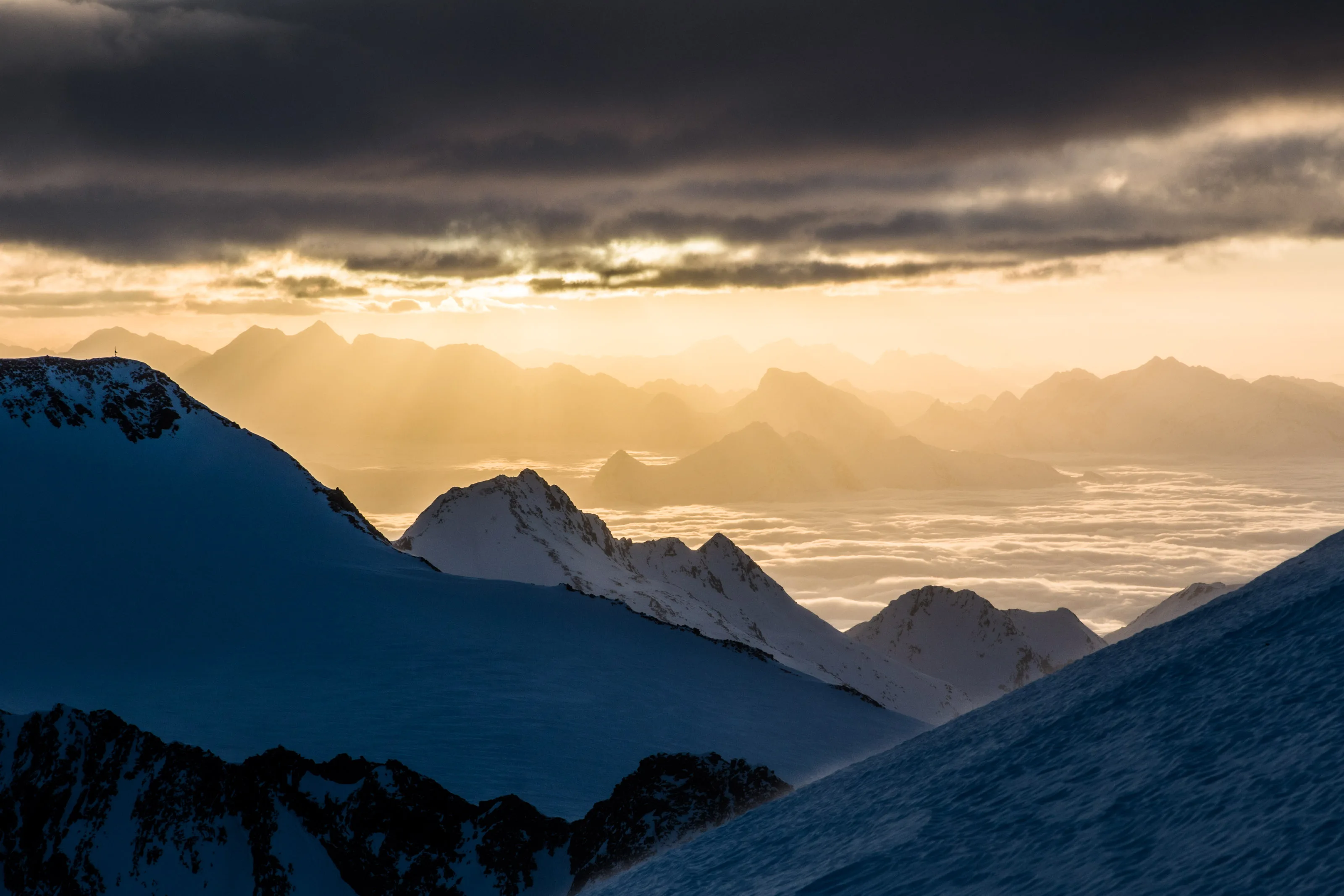 Sonnenlicht fällt durch Wolken auf die winterlichen Gipfel rund um den Stubaier Gletscher