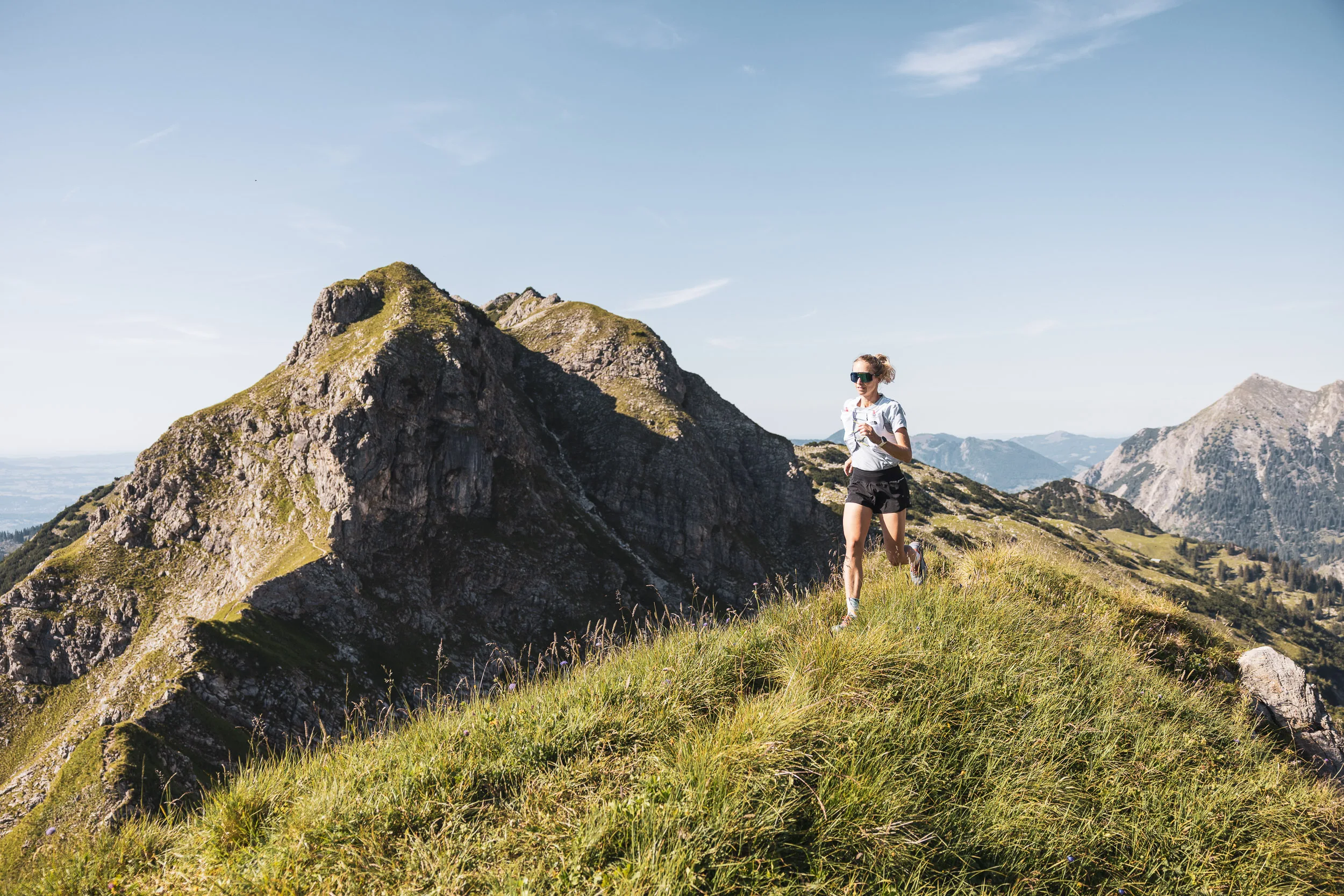 Ronja Morell läuft auf einem grasbewachsenen Berggrat vor den felsigen Allgäuer Alpen
