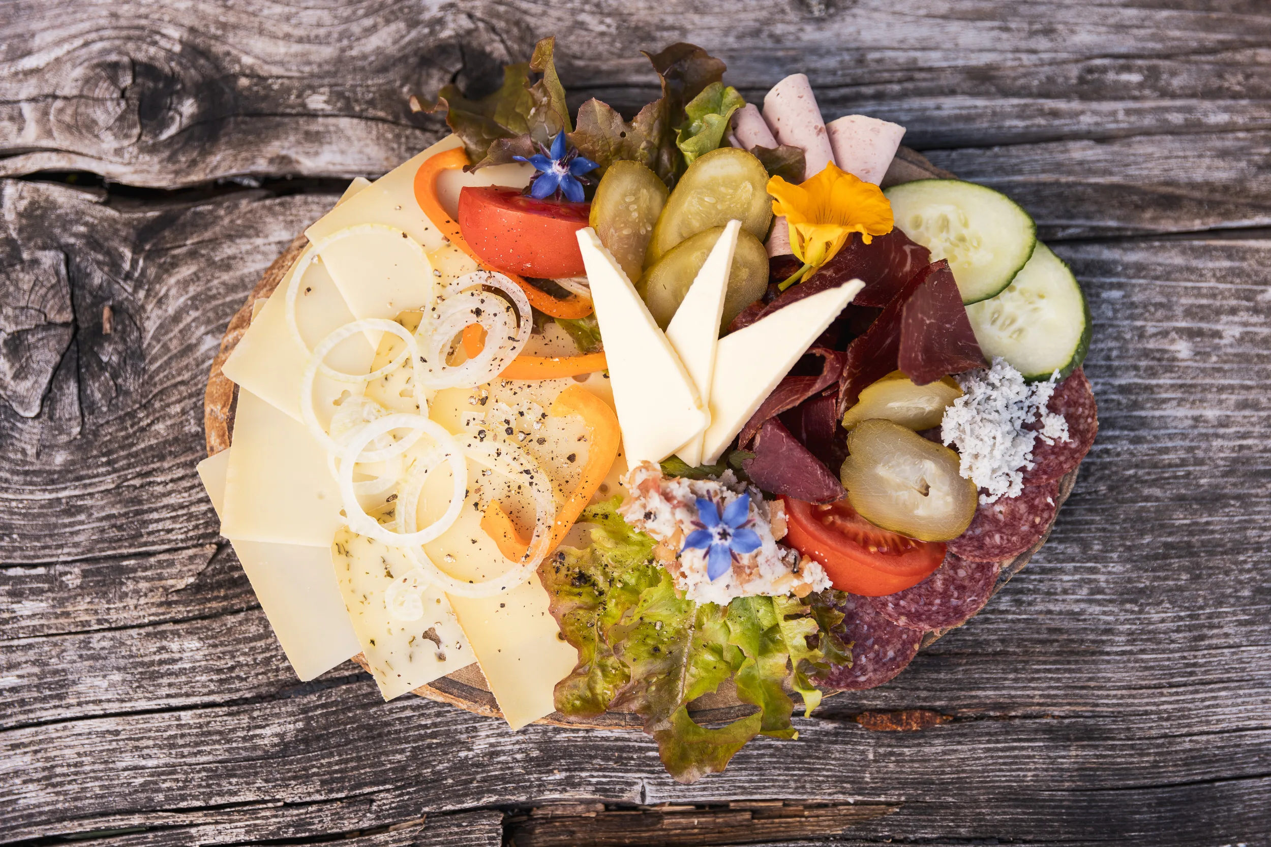 Allgäuer Brotzeit mit Käse, Gemüse und essbaren Blüten auf einem Holztisch