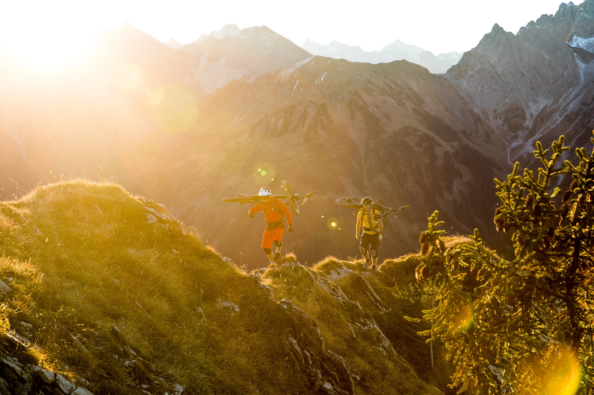 Mountainbiker mit ihren Rädern auf einem schmalen Bergkamm vor schroffen Alpen im Abendlicht