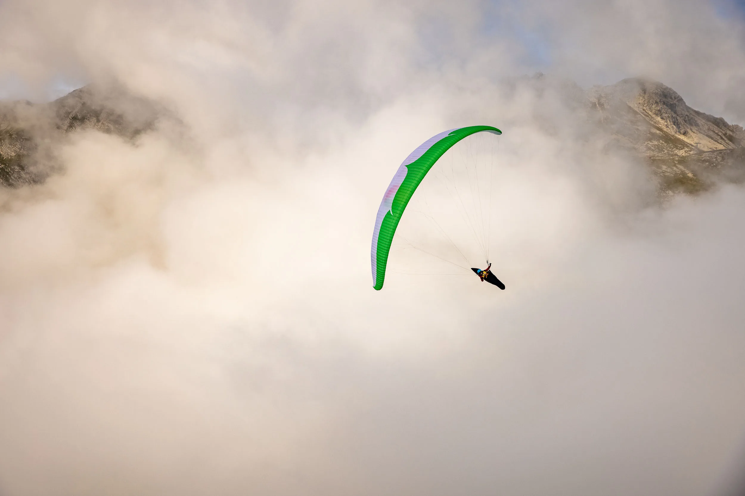 Klaudia Bulgakow fliegt mit ihrem grünen Gleitschirm vor Felswänden und Nebel am Nebelhorn.
