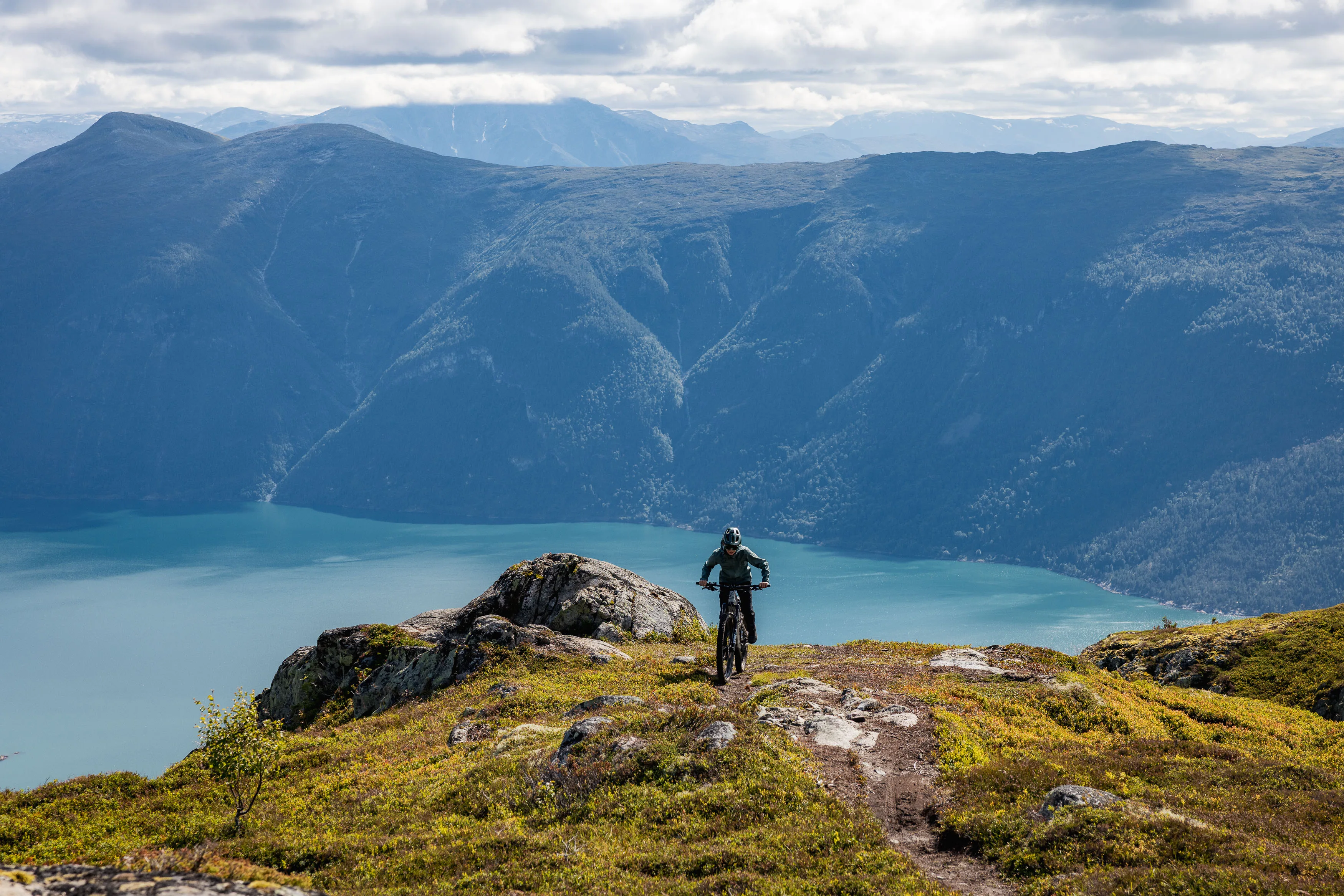 Mountainbiker fährt auf einem schmalen Höhenweg über einem weit verzweigten Fjord