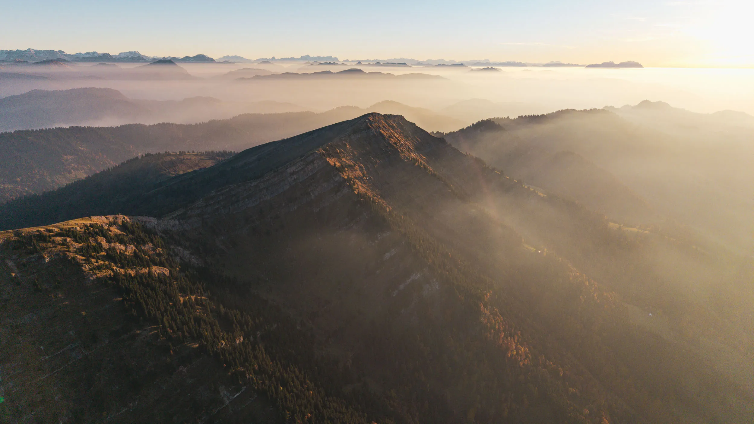 Warme Sonnenstrahlen liegen über gestaffelten Bergketten und Dunst im Tal