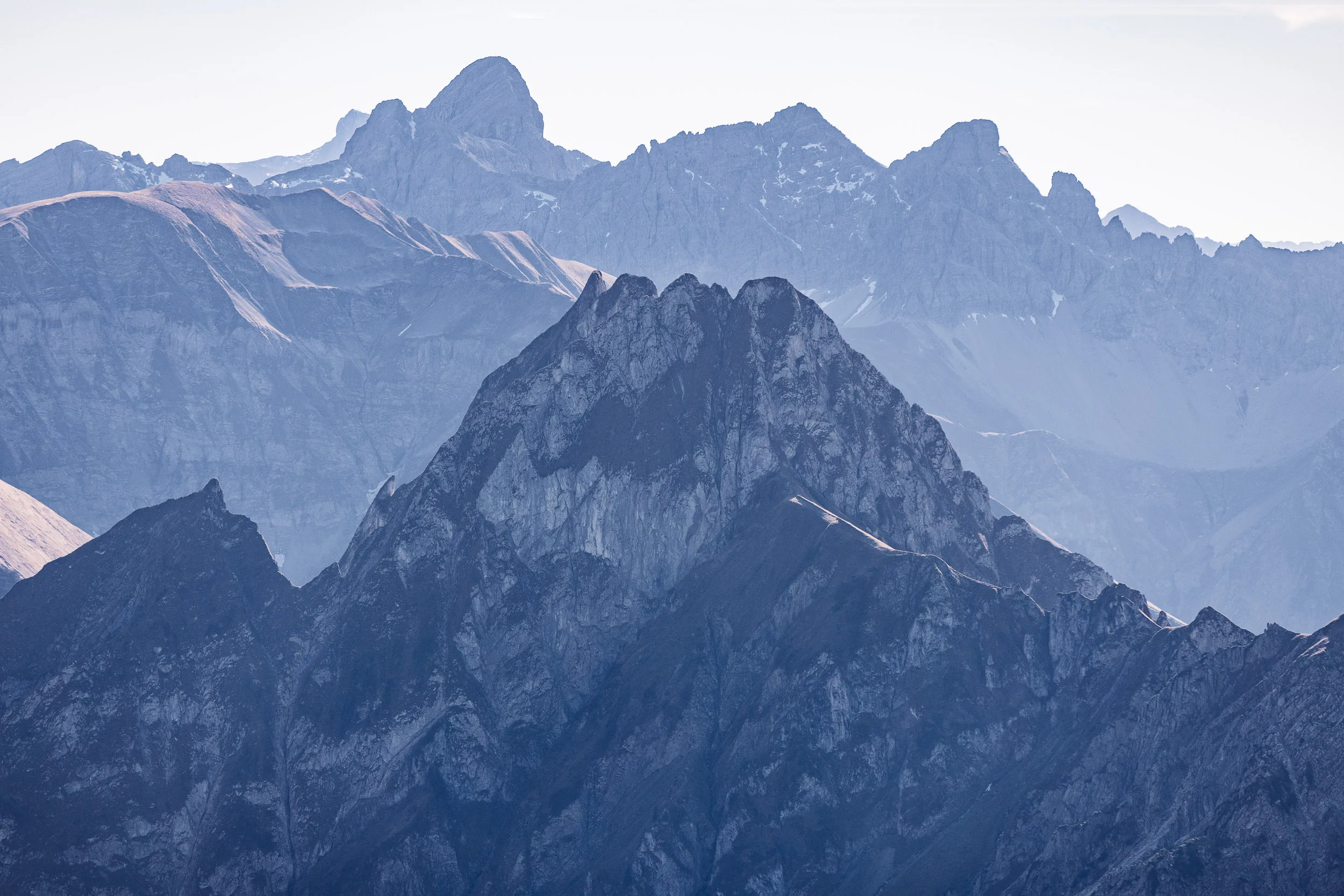 Dunkle Felsgipfel staffeln sich vor hellen Bergketten im herbstlichen Dunst.