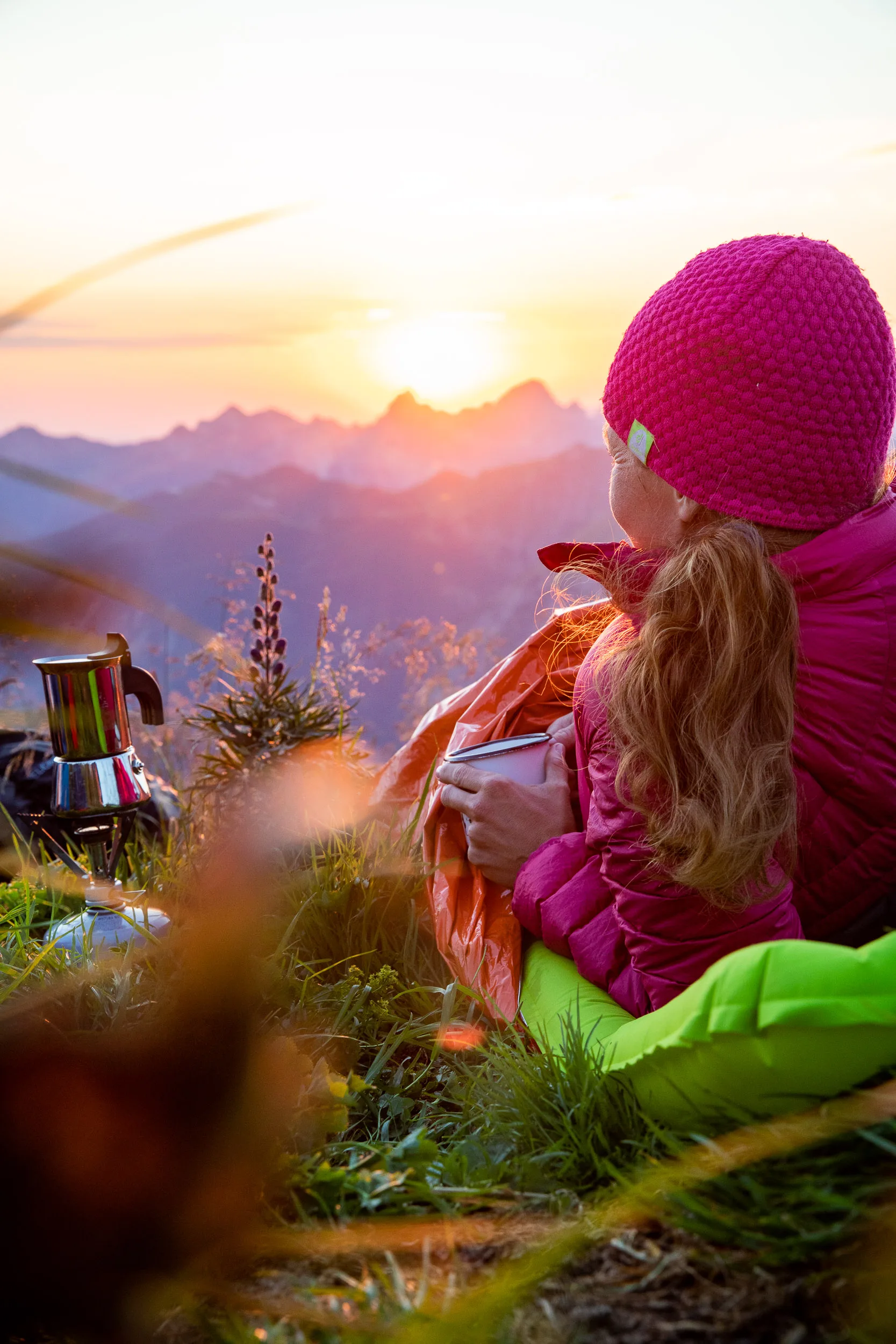 Caroline Nantke sitzt mit einer Tasse auf einer Bergwiese vor der tiefen Sonne