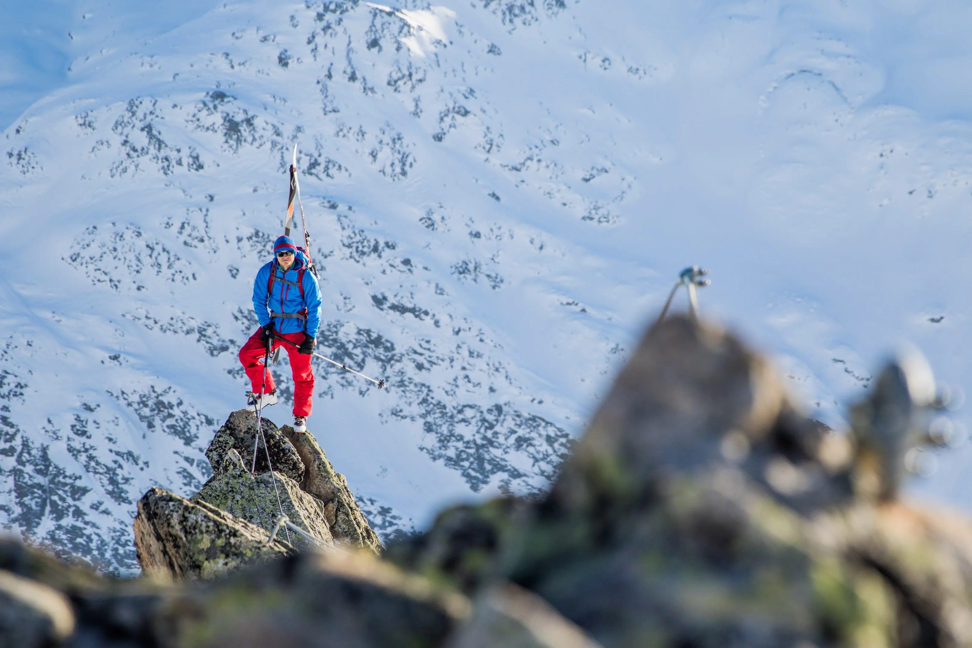 Ein Skitourengeher steht mit Tourenski auf einem Felsen vor einem winterlichen Bergpanorama
