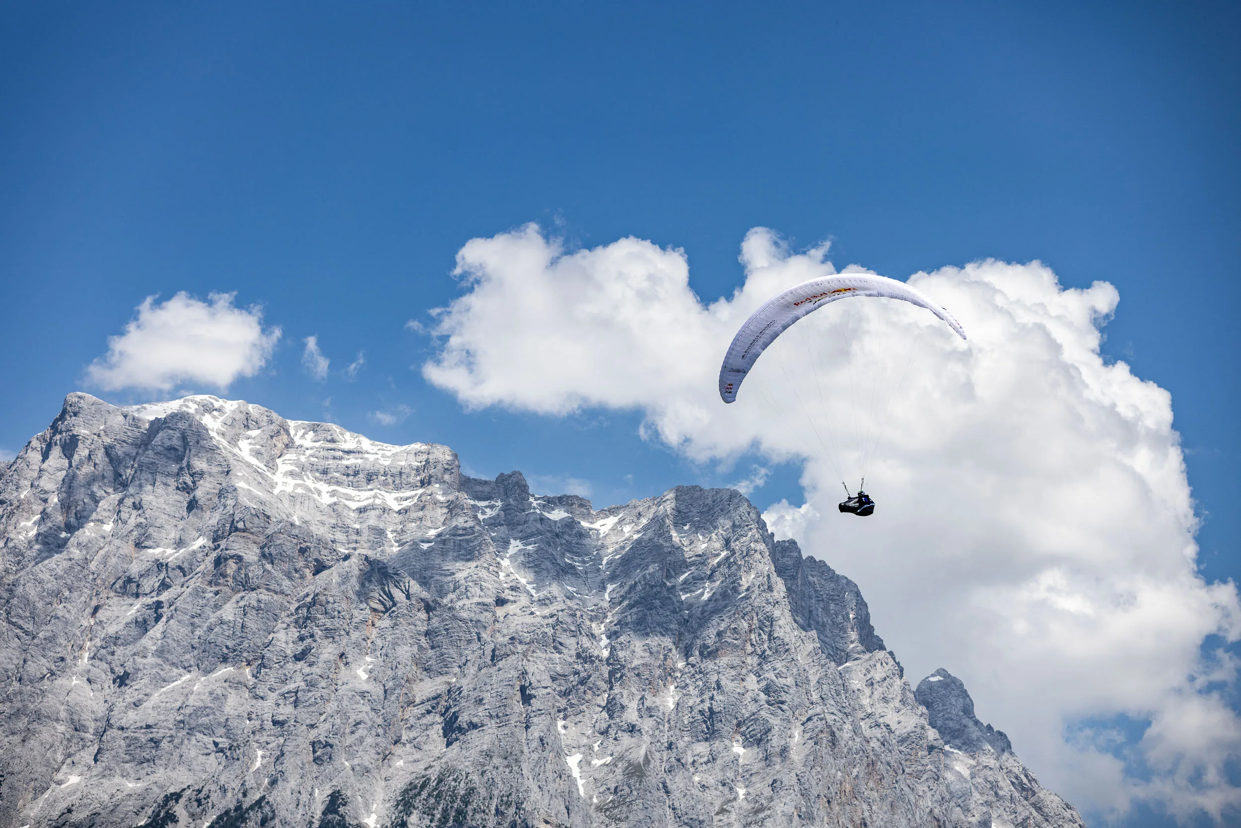 Eli Egger gleitet mit Gleitschirm vor der Zugspitze und großen Sommerwolken.