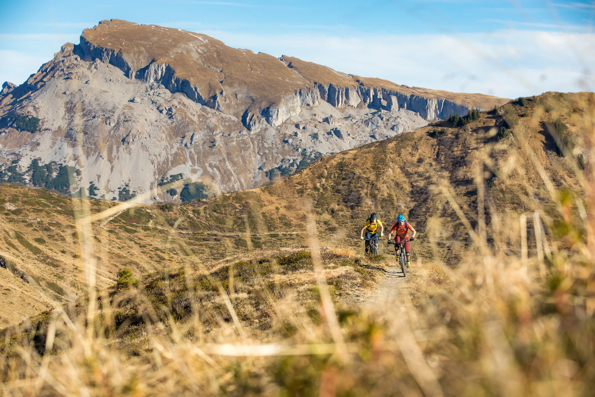 Drei Mountainbiker fahren über einen Hang vor einer hellen Felswand im Kleinwalsertal