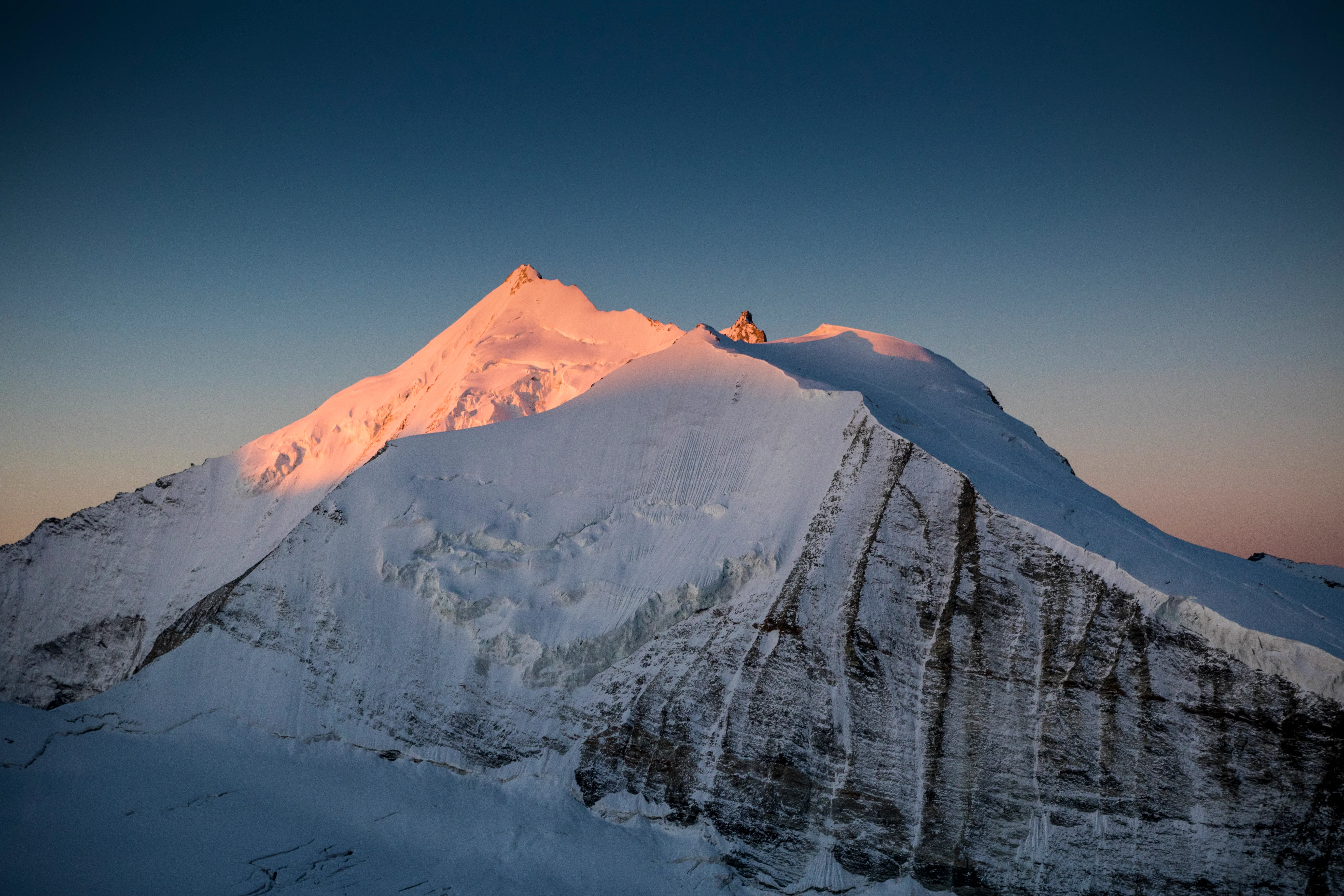 Warmes Abendlicht trifft einen verschneiten Gipfel oberhalb der Wolken im Wallis.