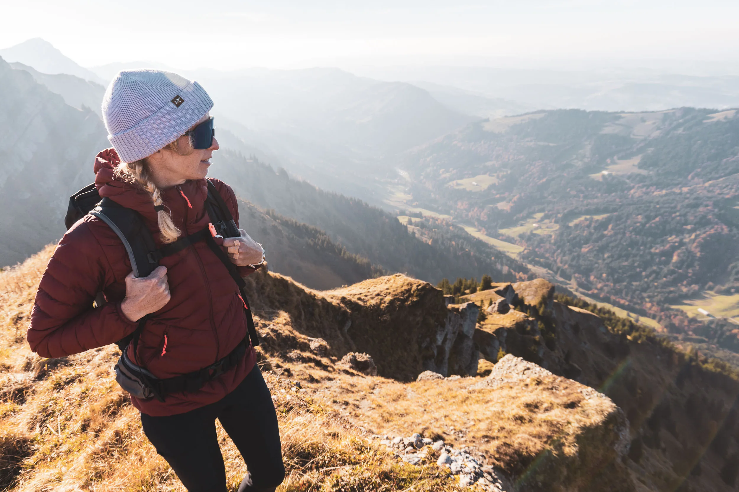 Wanderin steht mit Rucksack im warmen Licht vor der weiten Allgäuer Berglandschaft