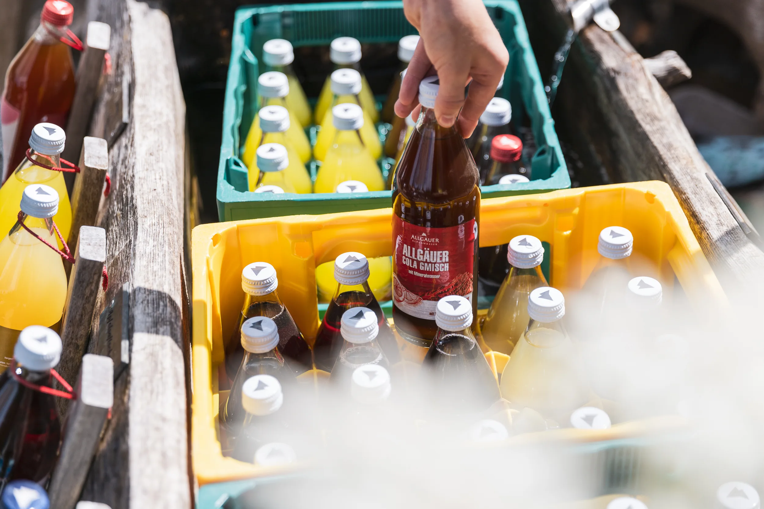 Eine Hand nimmt eine gekühlte Getränkeflasche aus dem Holztrog der Alpe