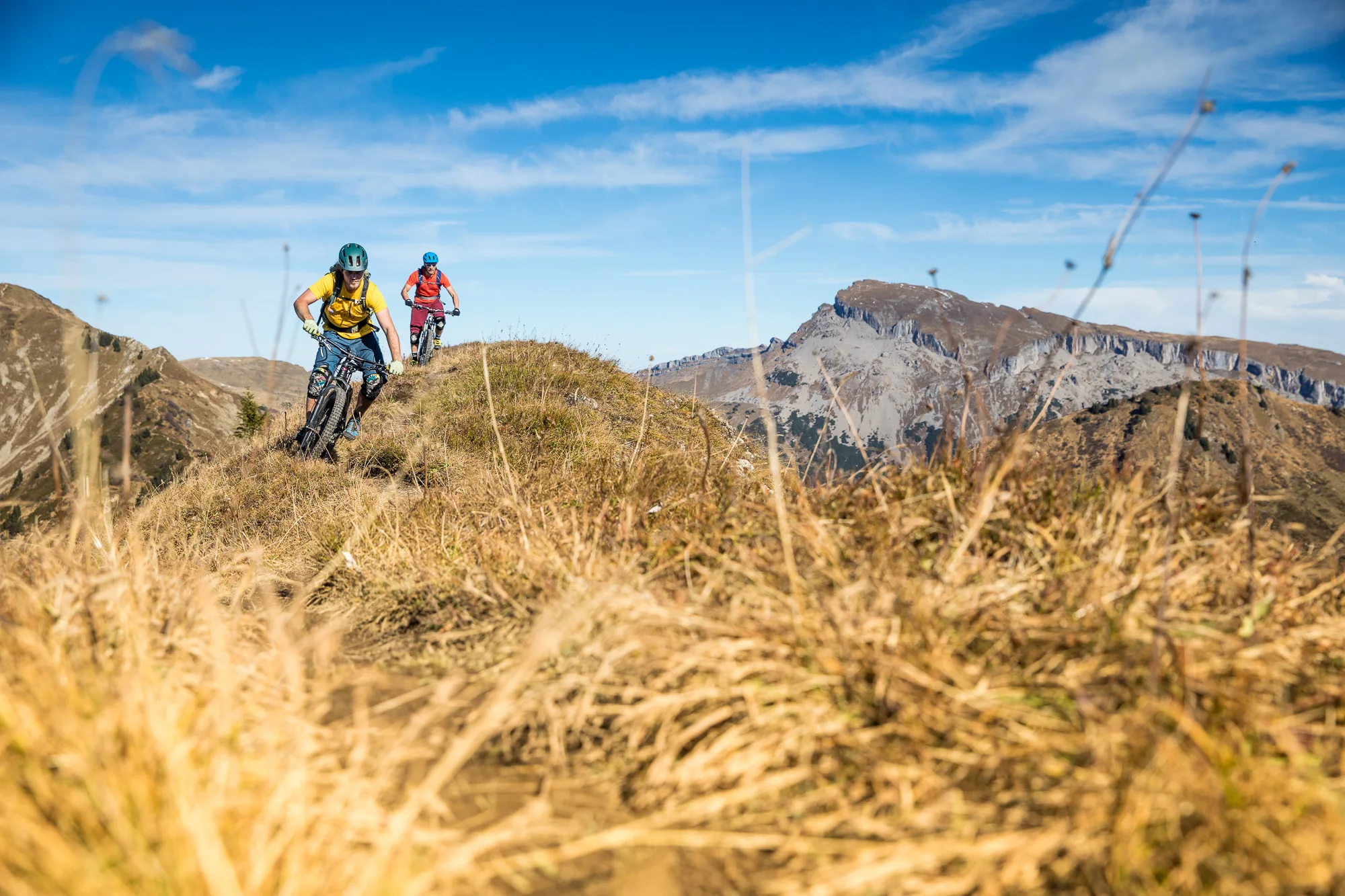 Zwei Mountainbiker fahren über eine offene Hochfläche mit felsigem Bergmassiv im Hintergrund