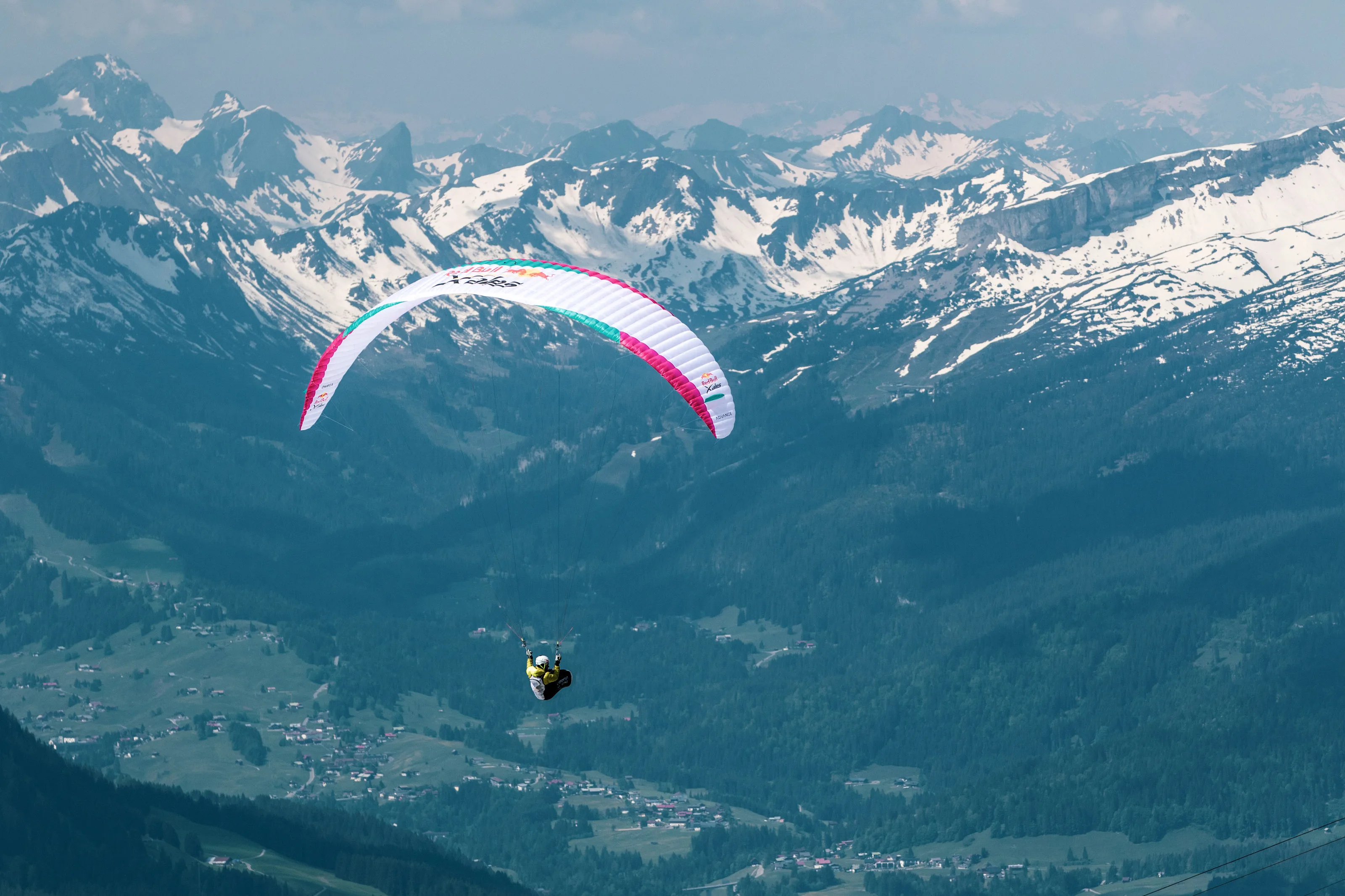 Michael Lacher fliegt unter einem pinkweißen Gleitschirm vor einer schneebedeckten Bergkette.