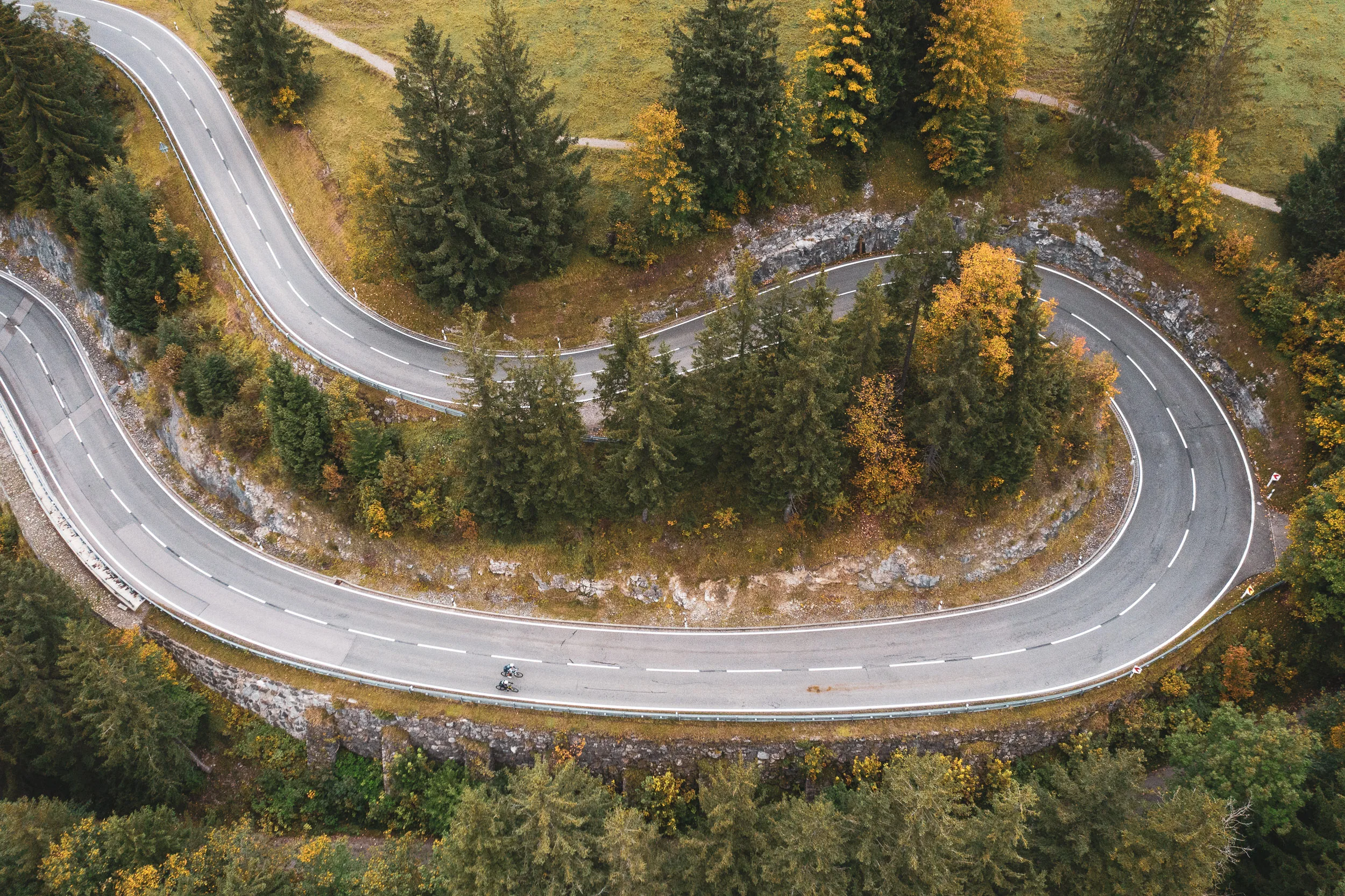 Ein Rennradfahrer fährt durch eine breite Kehre der Passstraße am Oberjoch im Herbst.