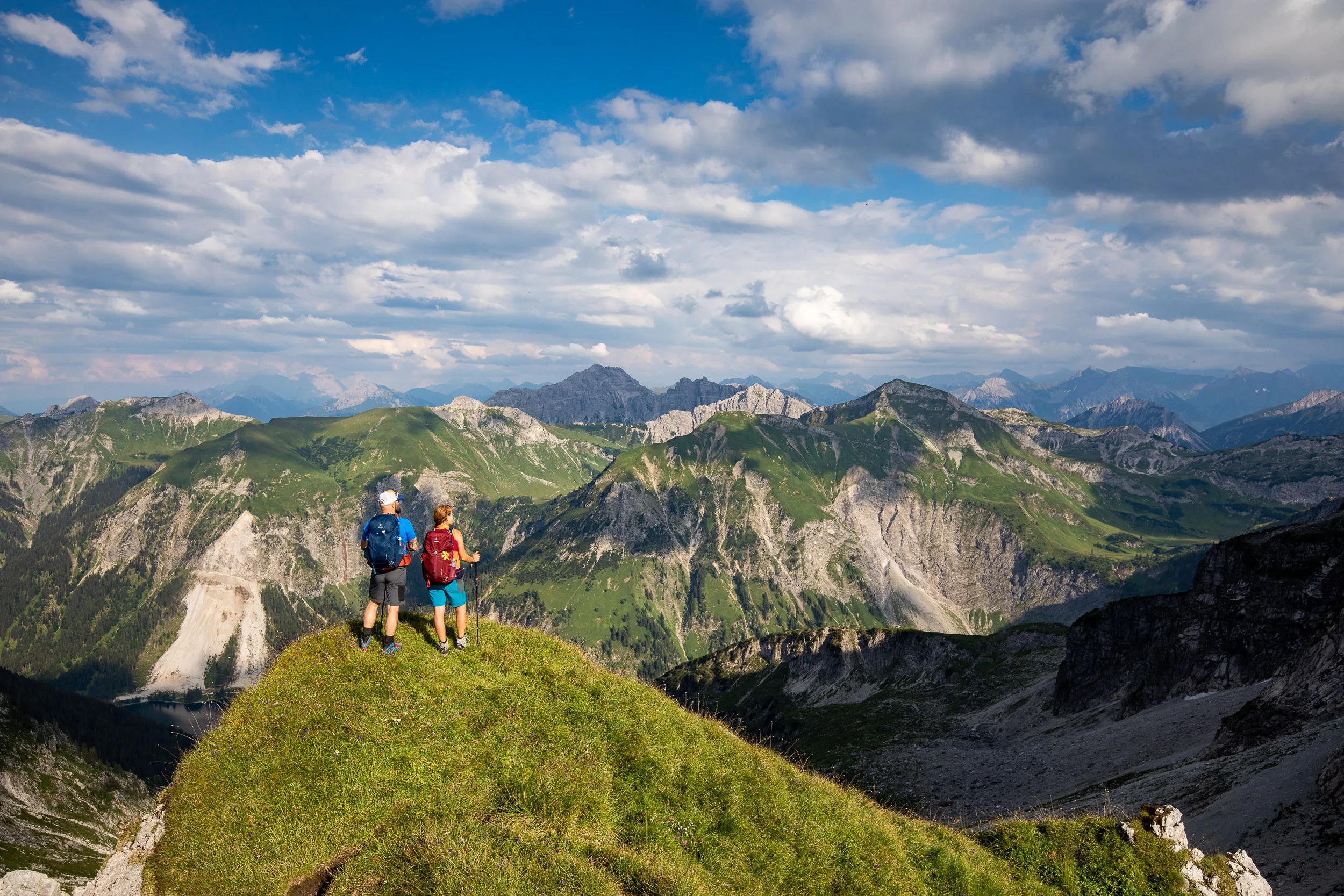 Caroline Nantke und Harald Dreyer blicken von einer grünen Gipfelkuppe in die Allgäuer Alpen